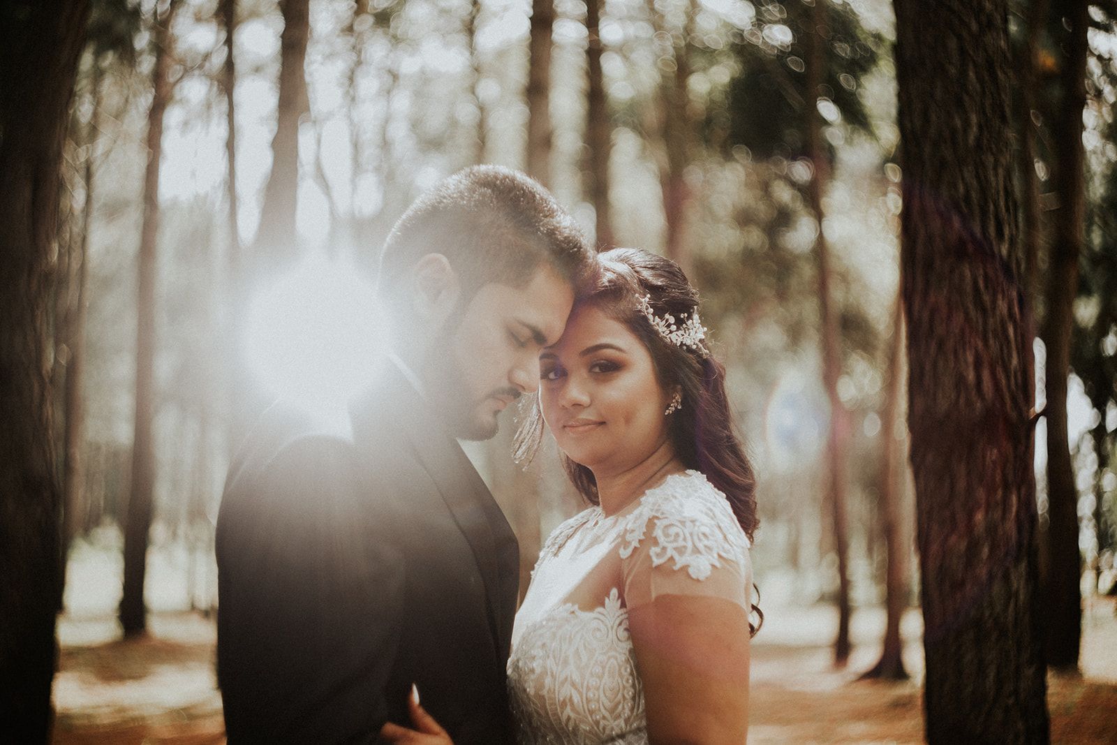 A bride and groom are posing for a picture in the woods.