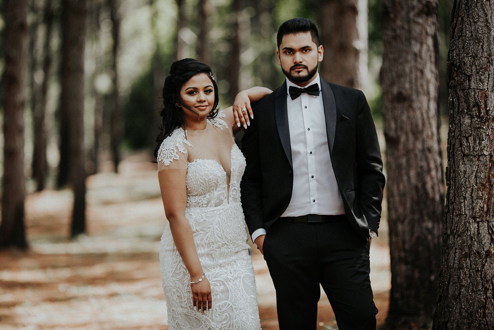 A bride and groom are posing for a picture in the woods.