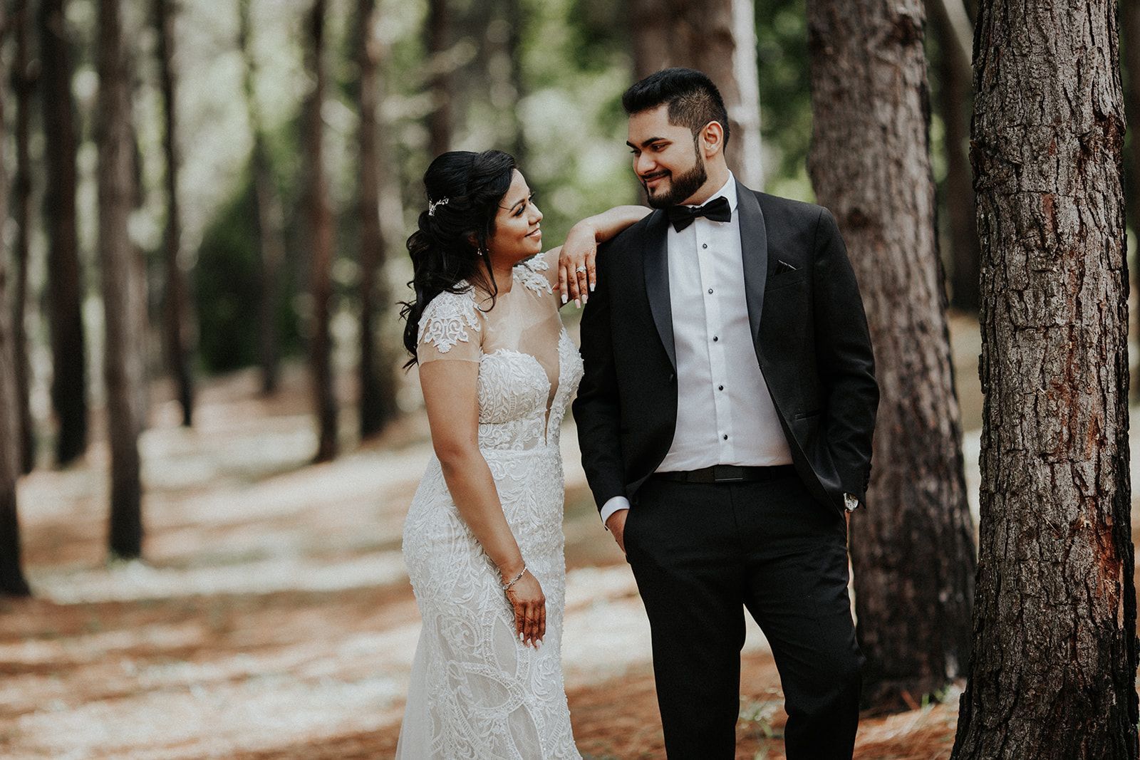 A bride and groom are standing next to each other in a forest.