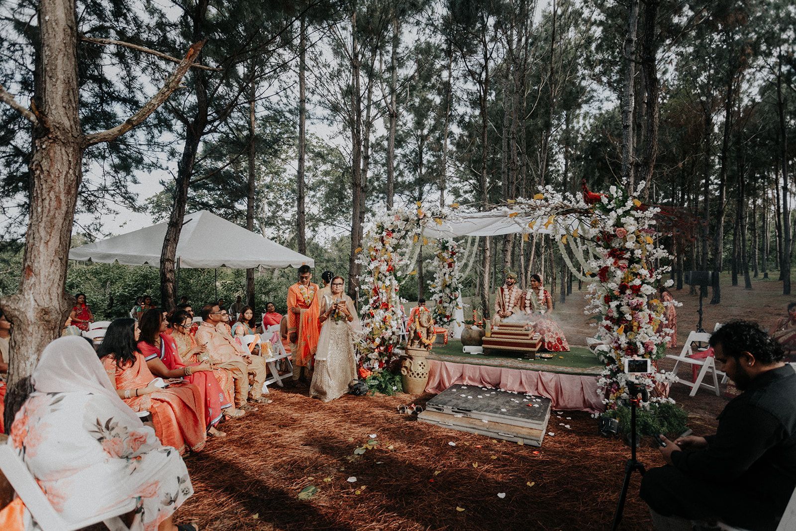 A man is taking a picture of a wedding ceremony in the woods.