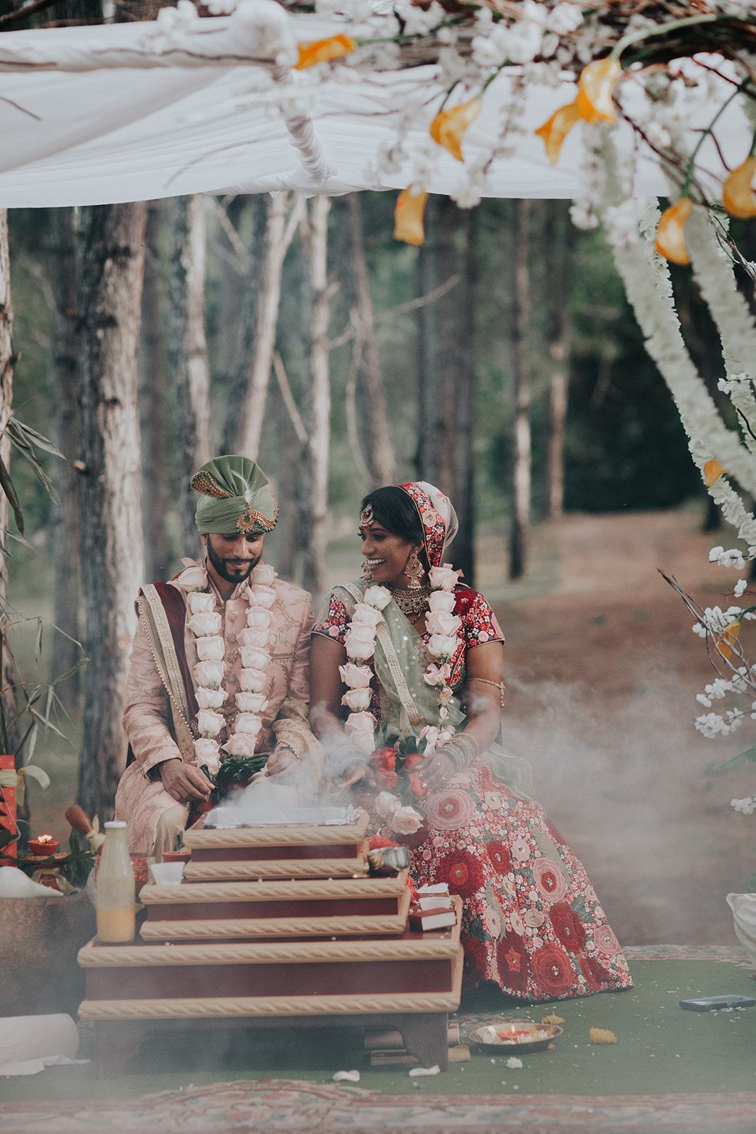 A bride and groom are sitting under a canopy in the woods during their wedding ceremony.