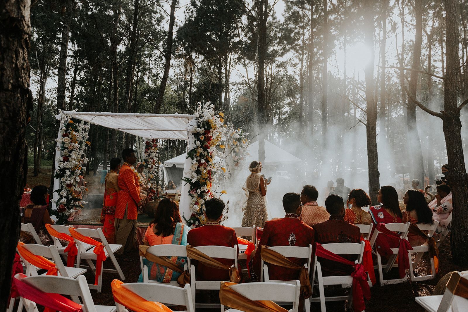 A group of people are sitting in chairs at a wedding ceremony in the woods.