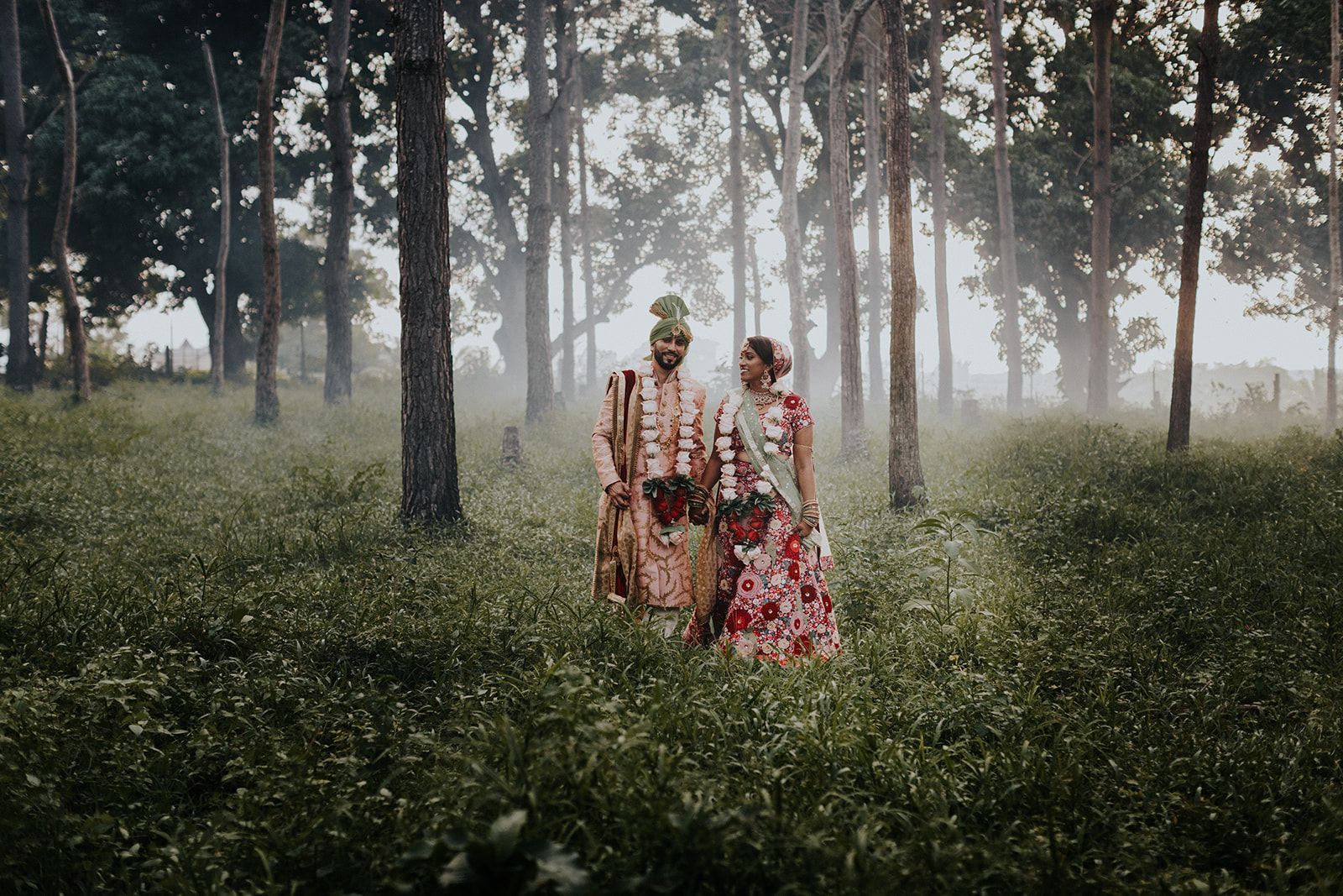 A bride and groom are standing in the middle of a forest.