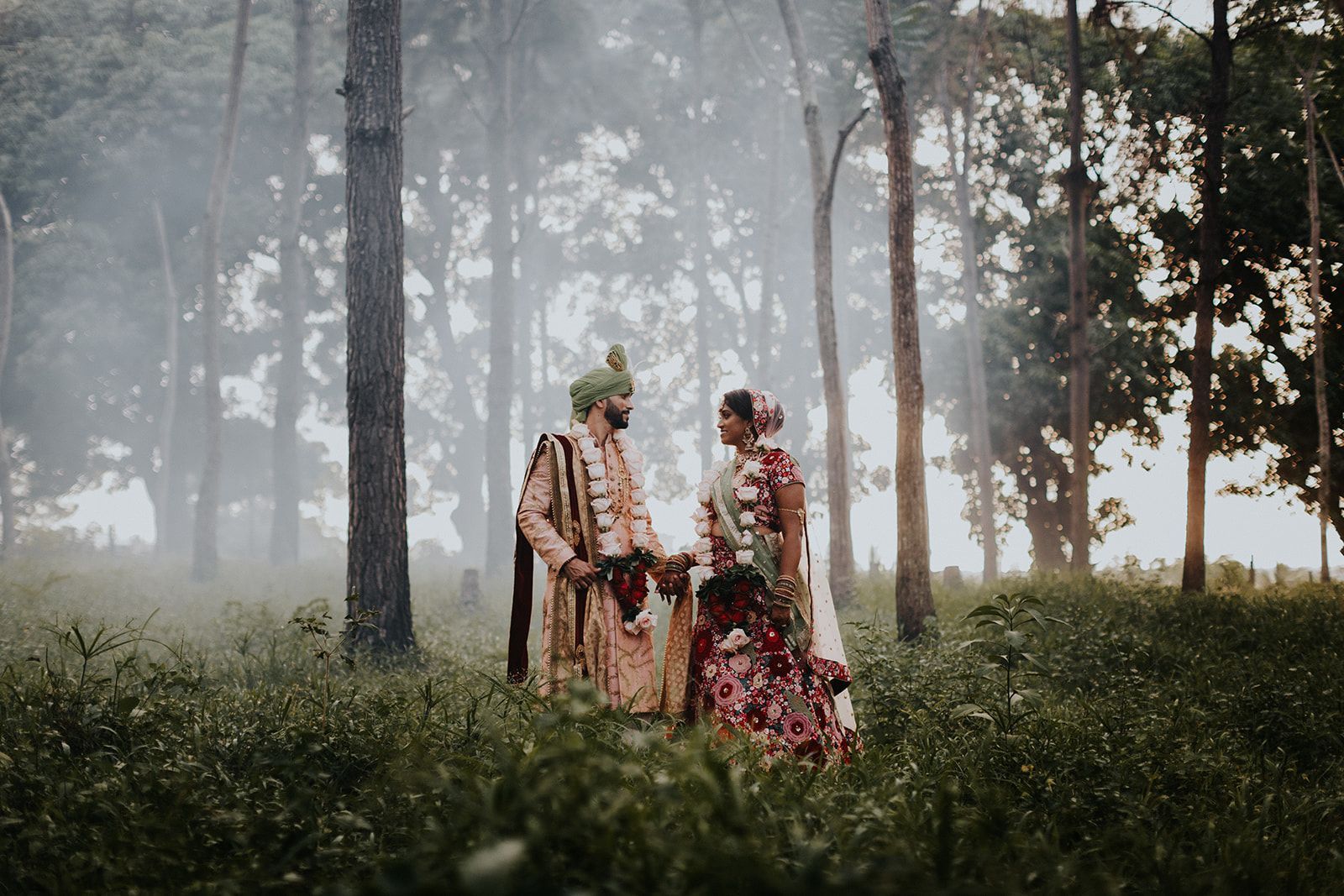 A bride and groom are standing in the middle of a forest holding hands.