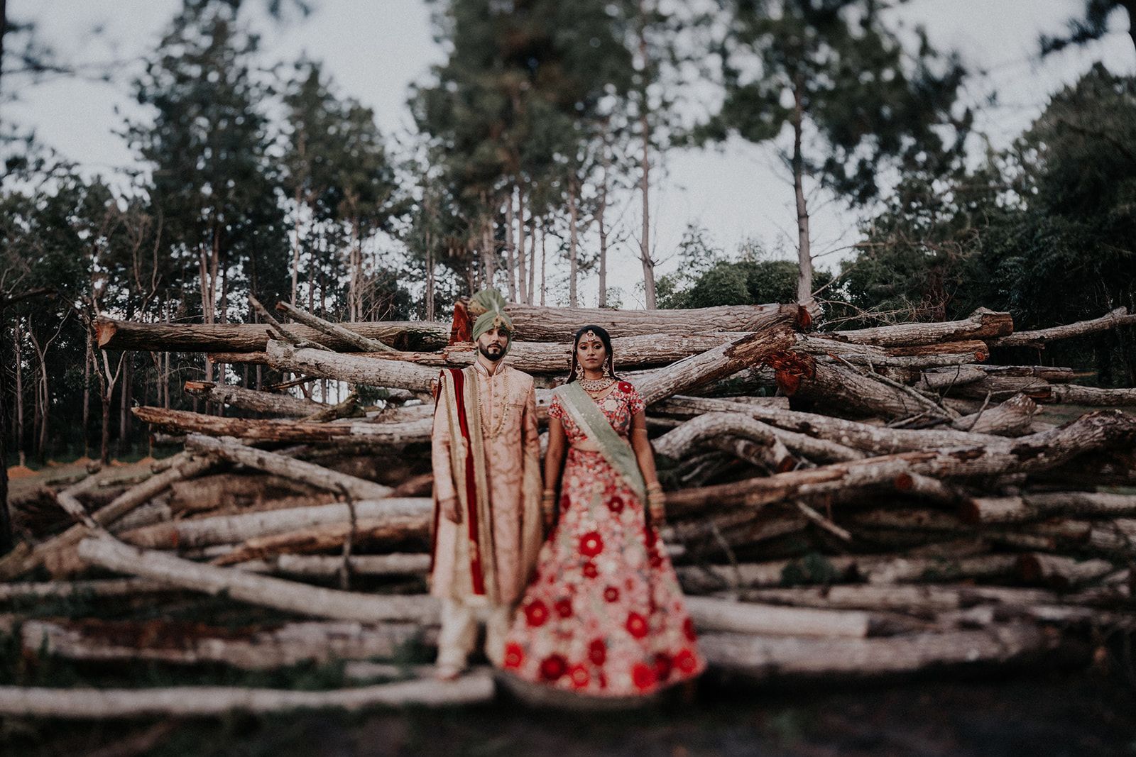 A bride and groom are standing in front of a pile of logs.