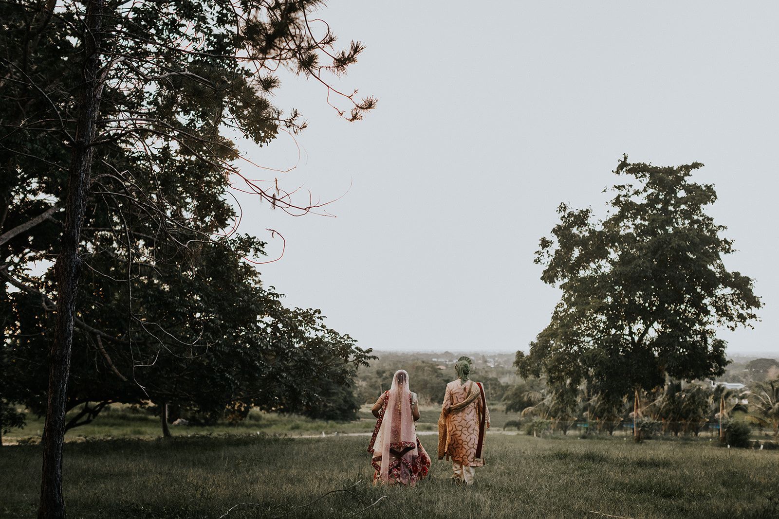 Two women are walking in a field with trees in the background.