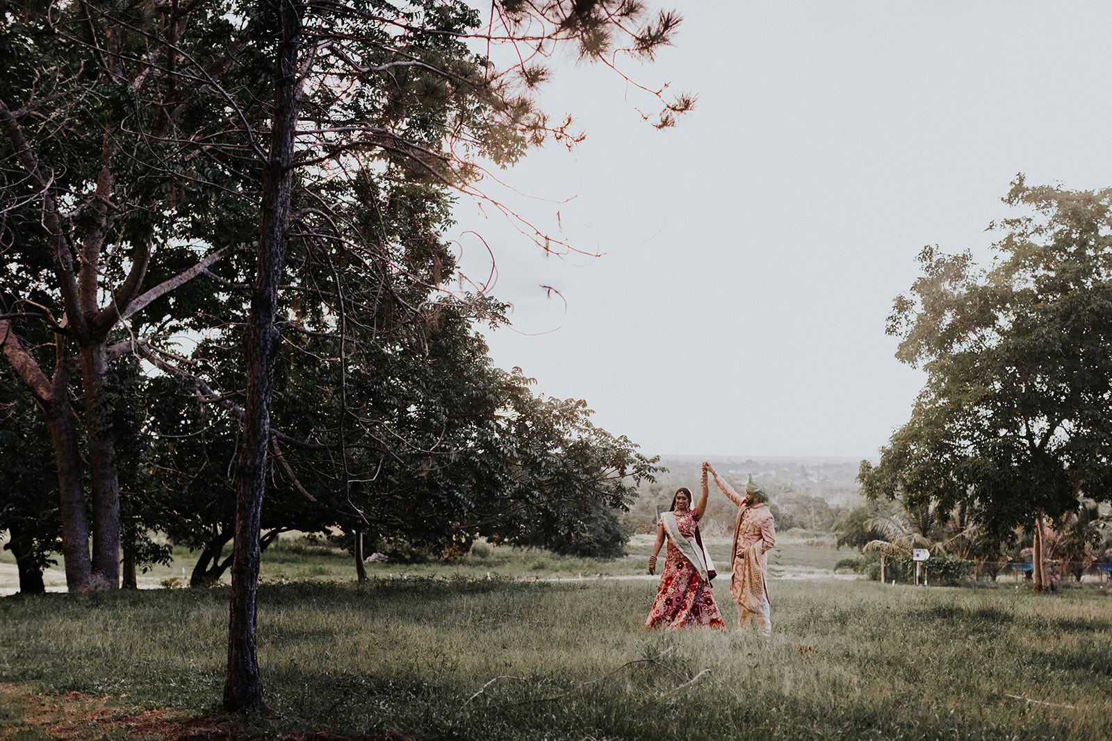 Two women are standing in a grassy field with trees in the background.