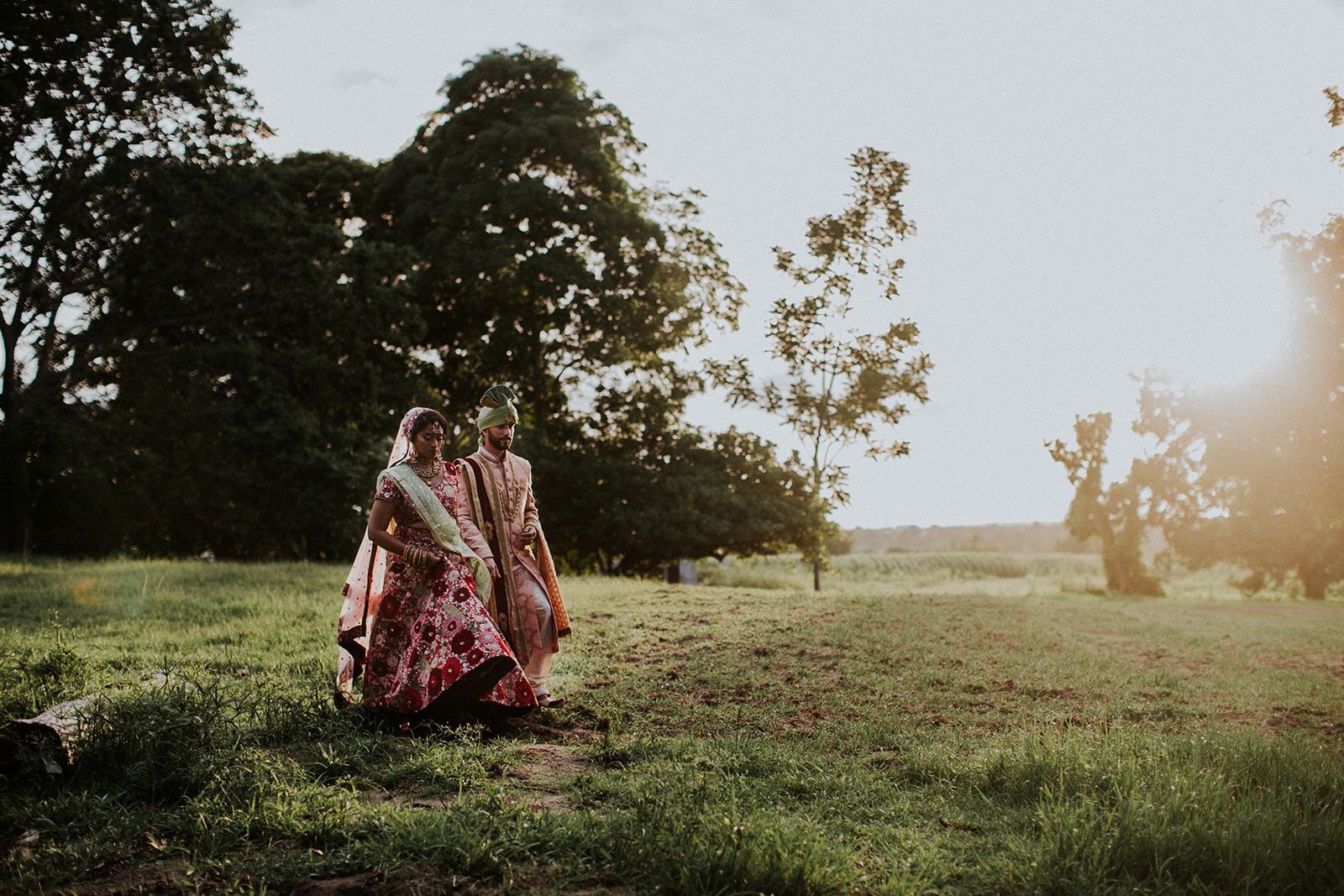 A bride and groom are walking through a grassy field.