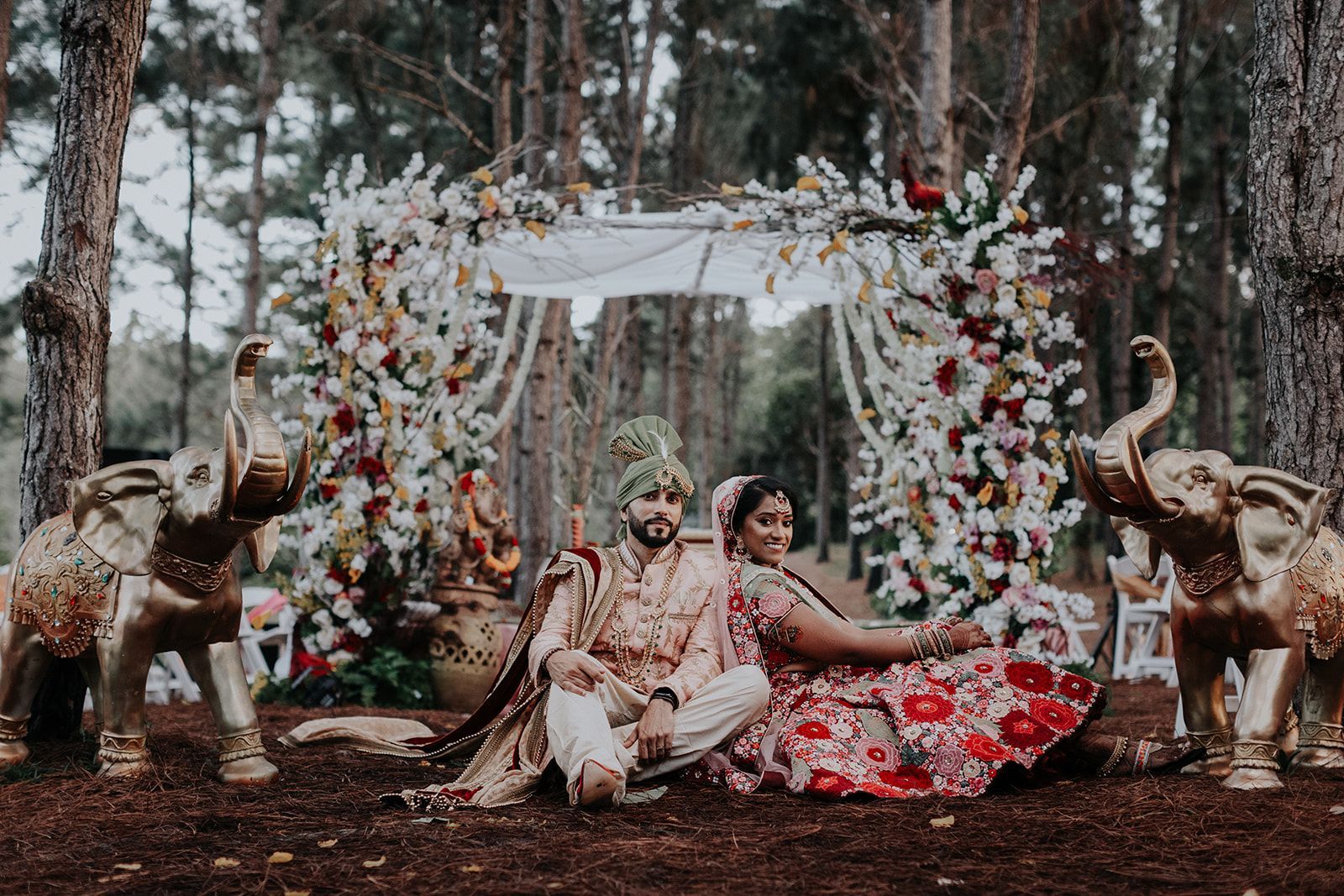 A bride and groom are sitting under a canopy in the woods surrounded by elephant statues.