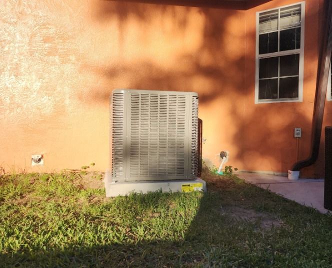 A large air conditioner is sitting in the grass in front of a house.