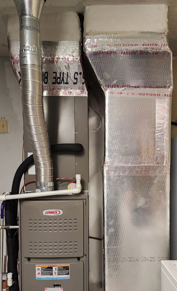 A furnace is sitting in a basement next to a duct.