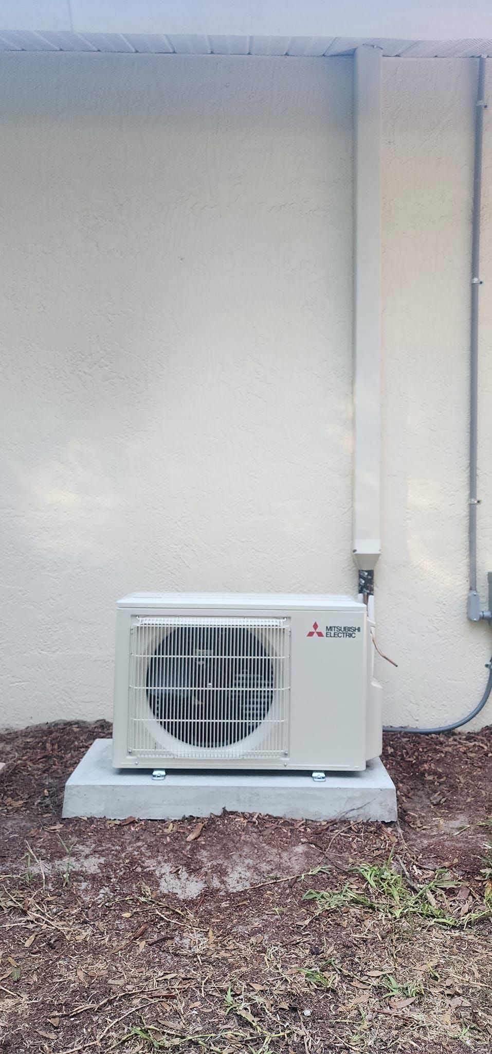 A white air conditioner is sitting on a concrete base in front of a white wall.