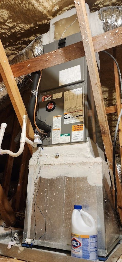 An air conditioner is sitting in the attic next to a bleach bottle.