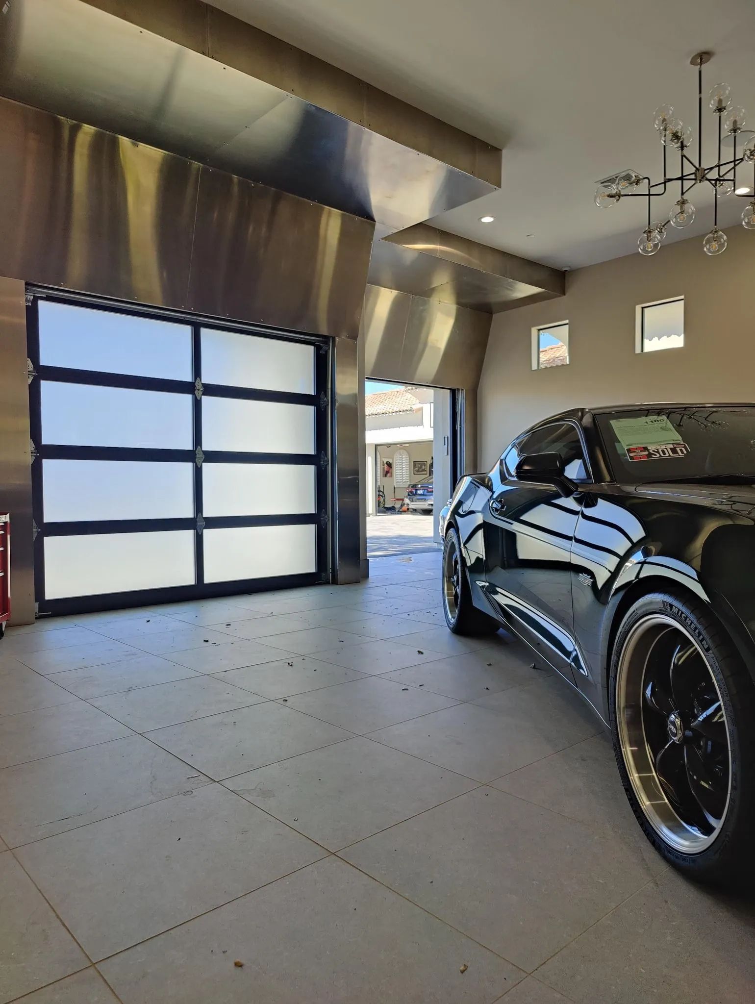 Modern glass panel garage door with a black sports car parked inside a stylish garage.