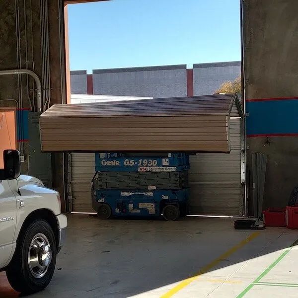 Genie lift with a large metal structure on top, inside a warehouse or industrial building.