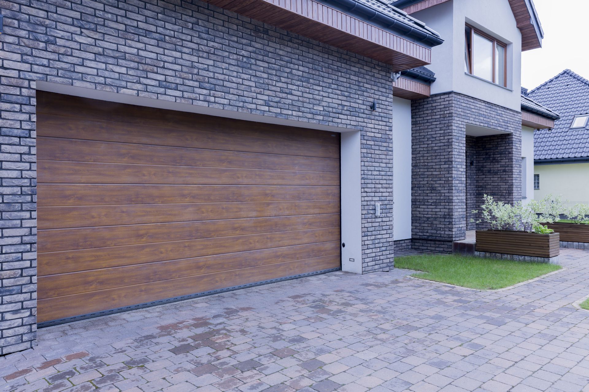 A contemporary house exterior featuring a wide, closed sectional garage door with a warm wood-look f