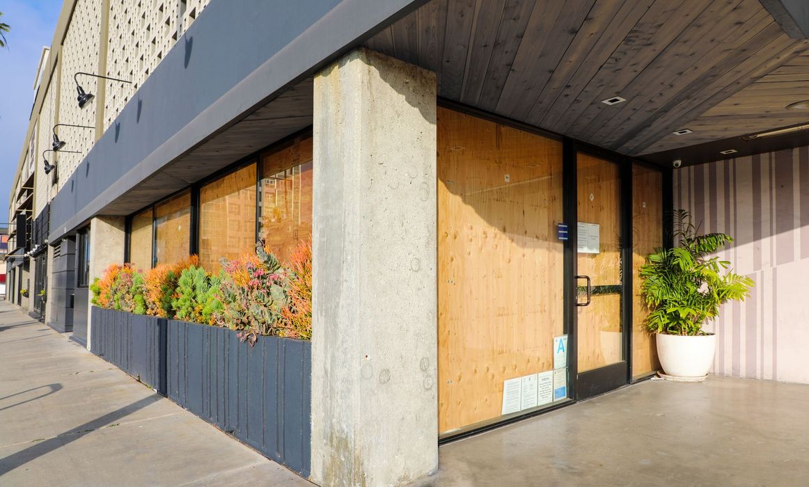 Exterior of a boarded-up building with planters of succulents and a potted plant.
