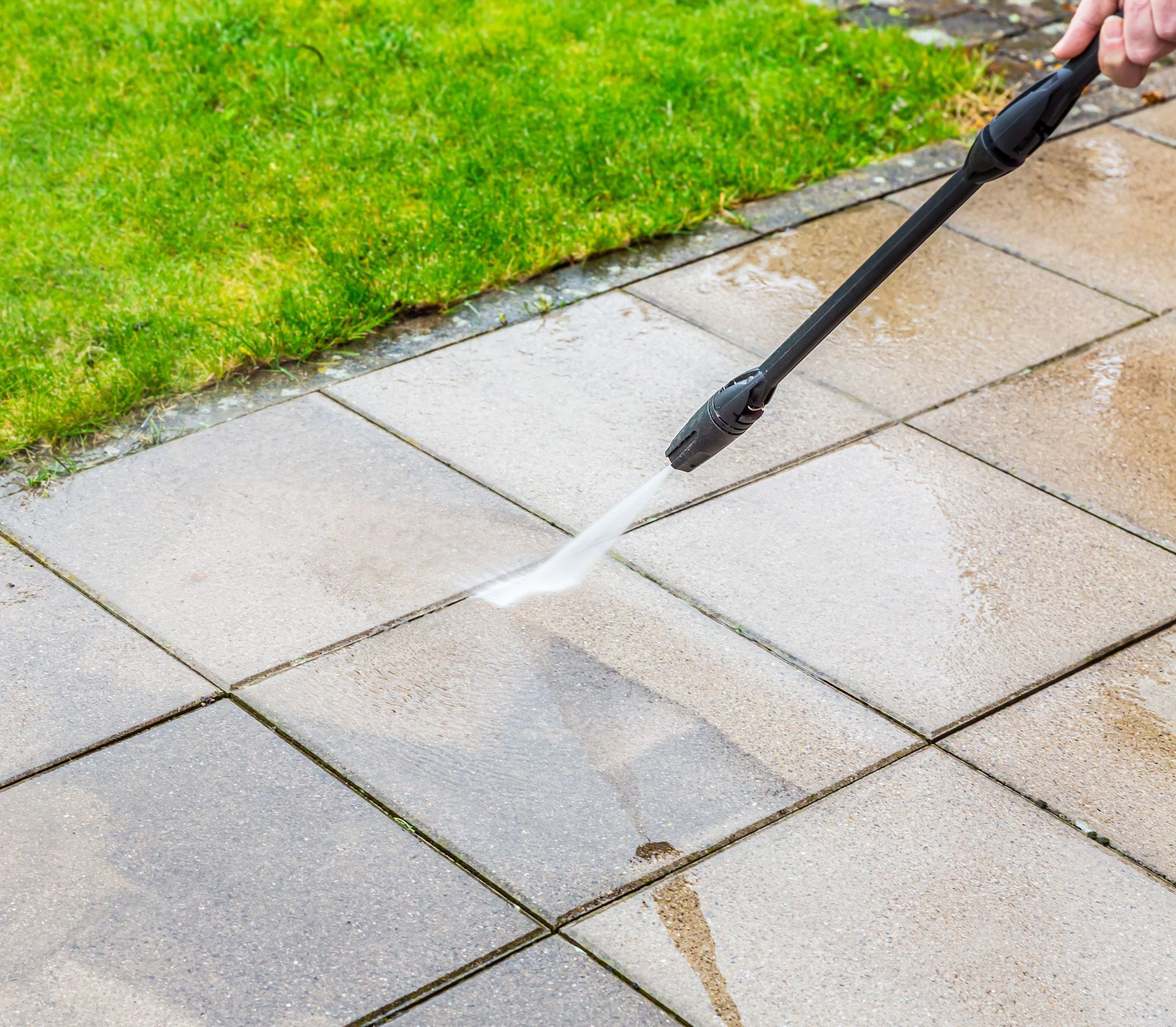 A person is using a high pressure washer to clean a patio.