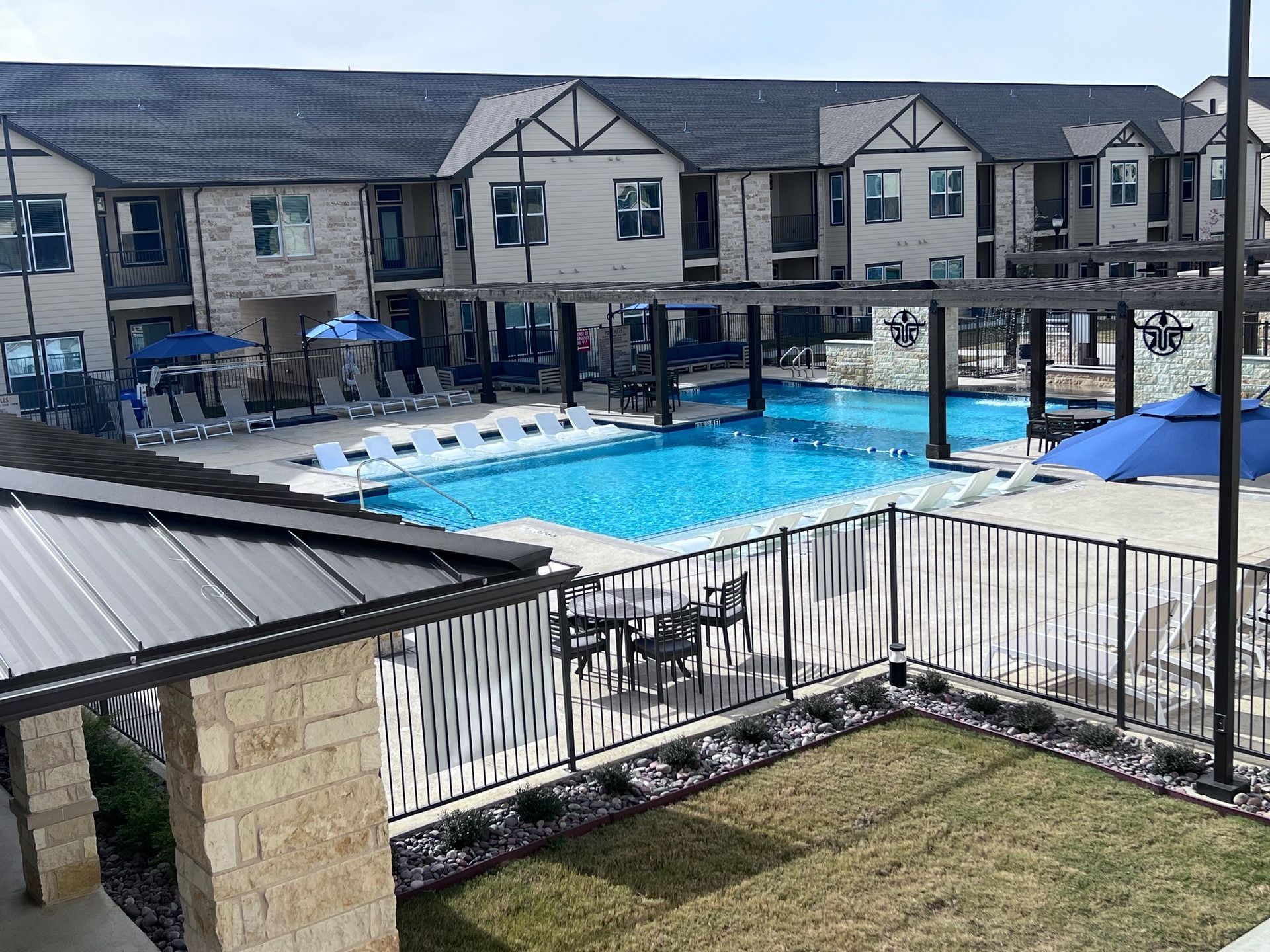 A pool area with lounge chairs, tables, and umbrellas. Buildings surround the pool.