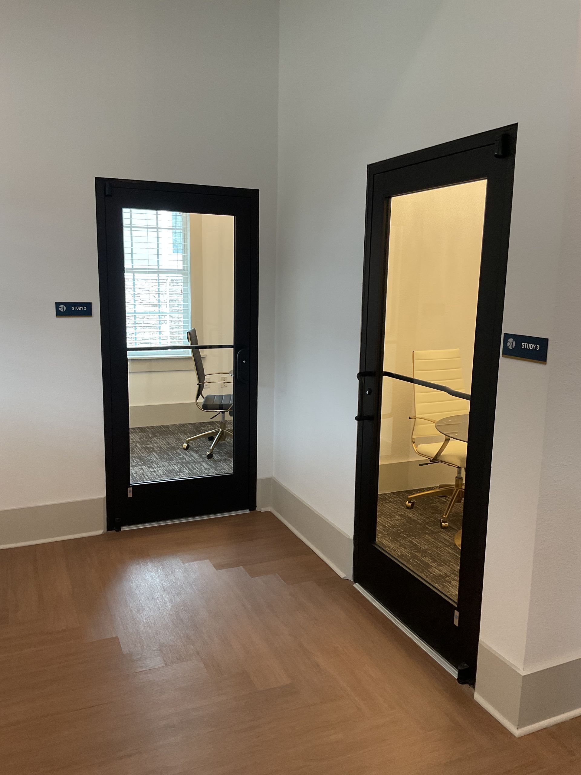 Two black-framed glass doors in a corner. One door is open, showing an office interior; the other is closed.