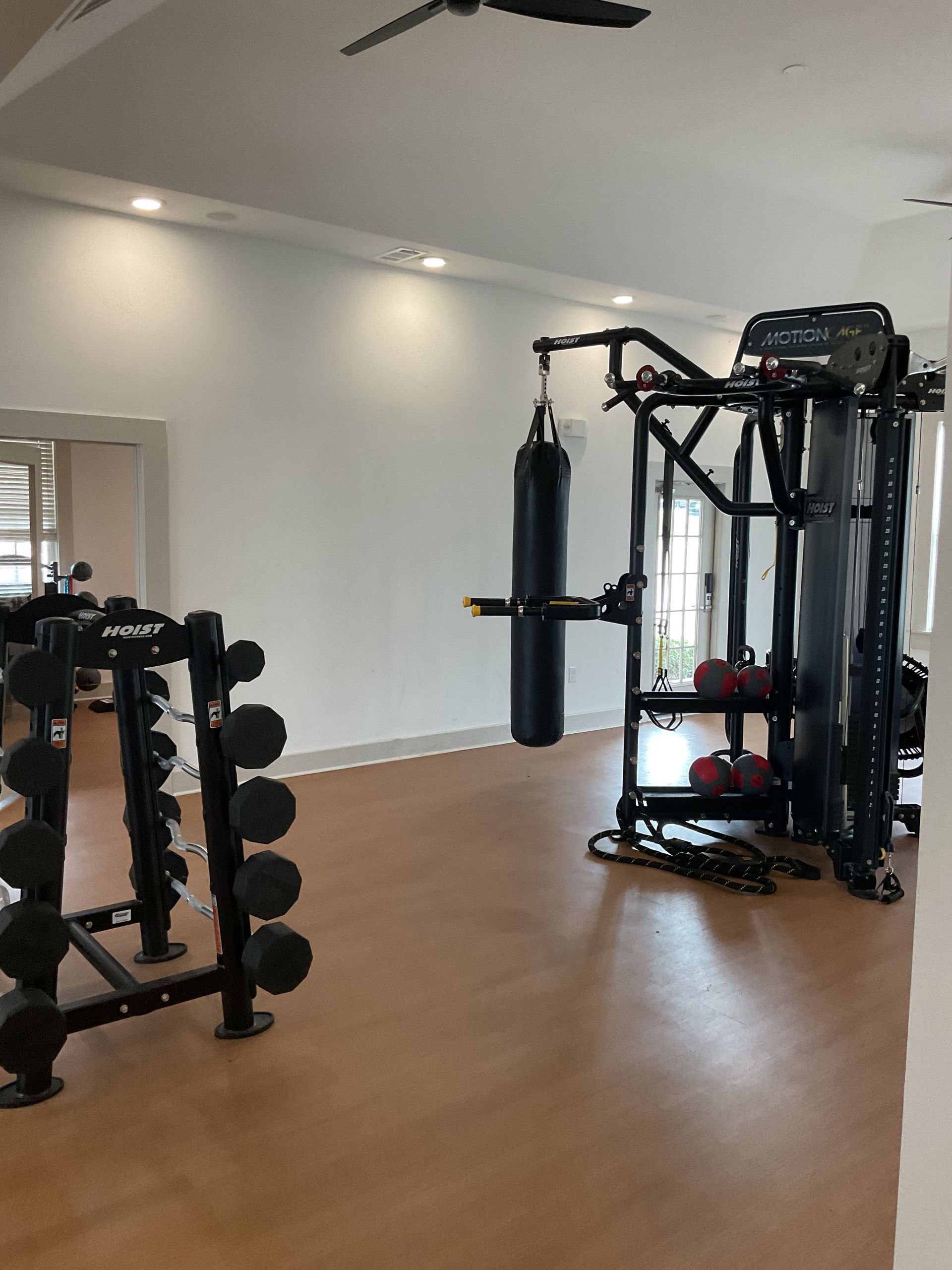 Gym interior with weight racks, punching bag, and multi-gym equipment. Beige flooring and white walls.