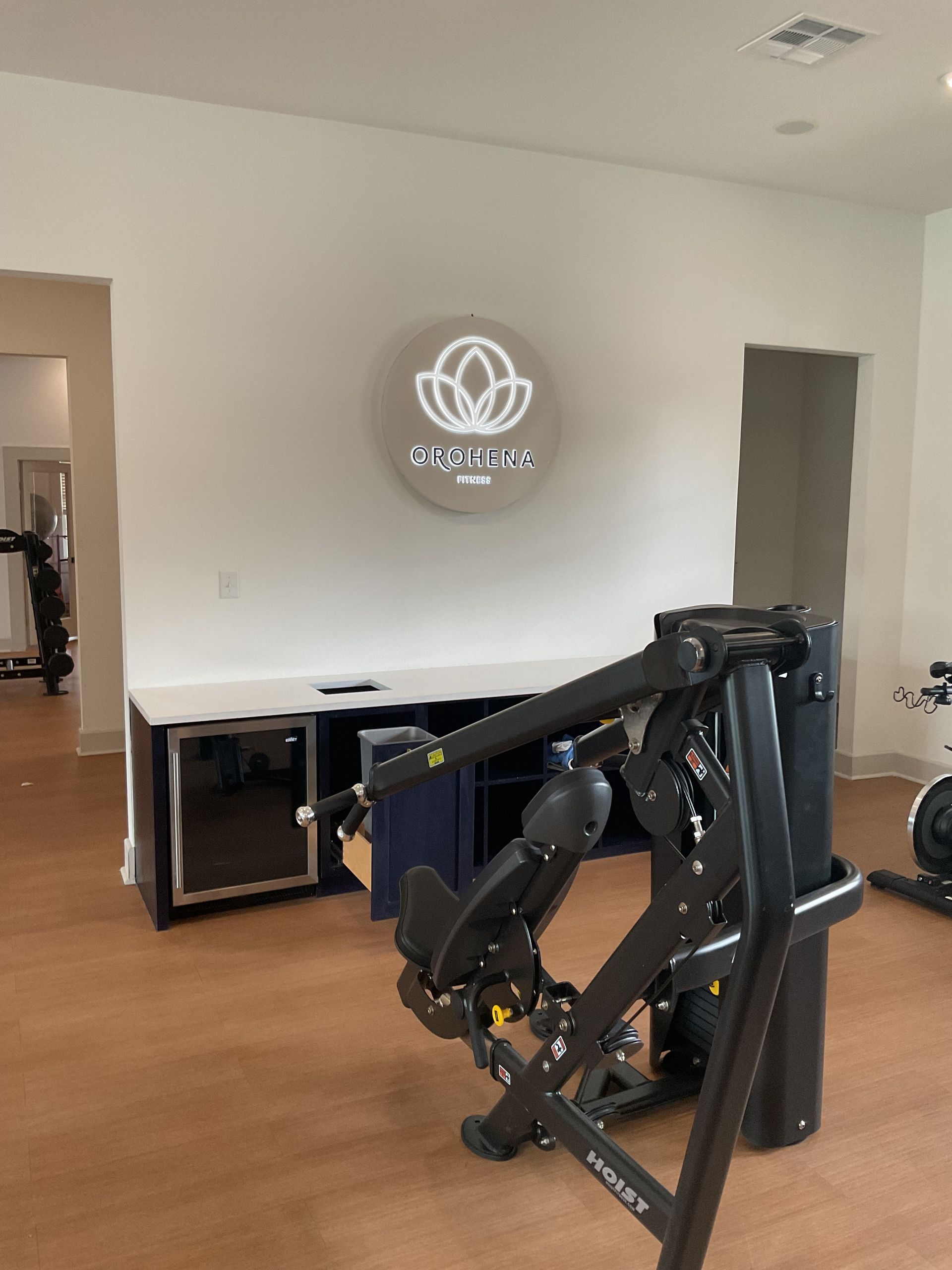 Gym interior with exercise equipment and a logo on the wall. Brown floor, white walls.