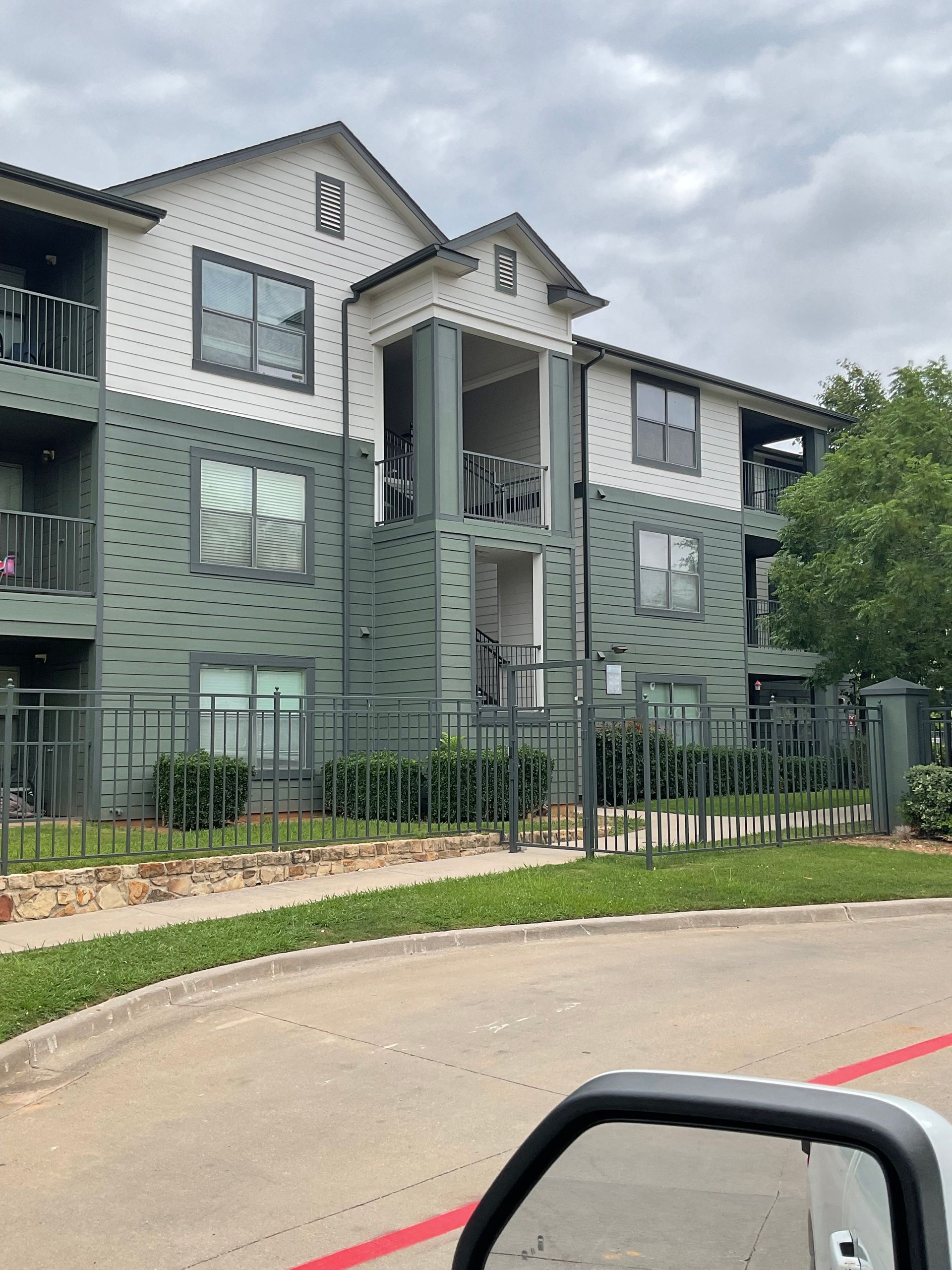 Apartment building with green and white exterior, windows, balcony, and a wrought-iron fence under a cloudy sky.