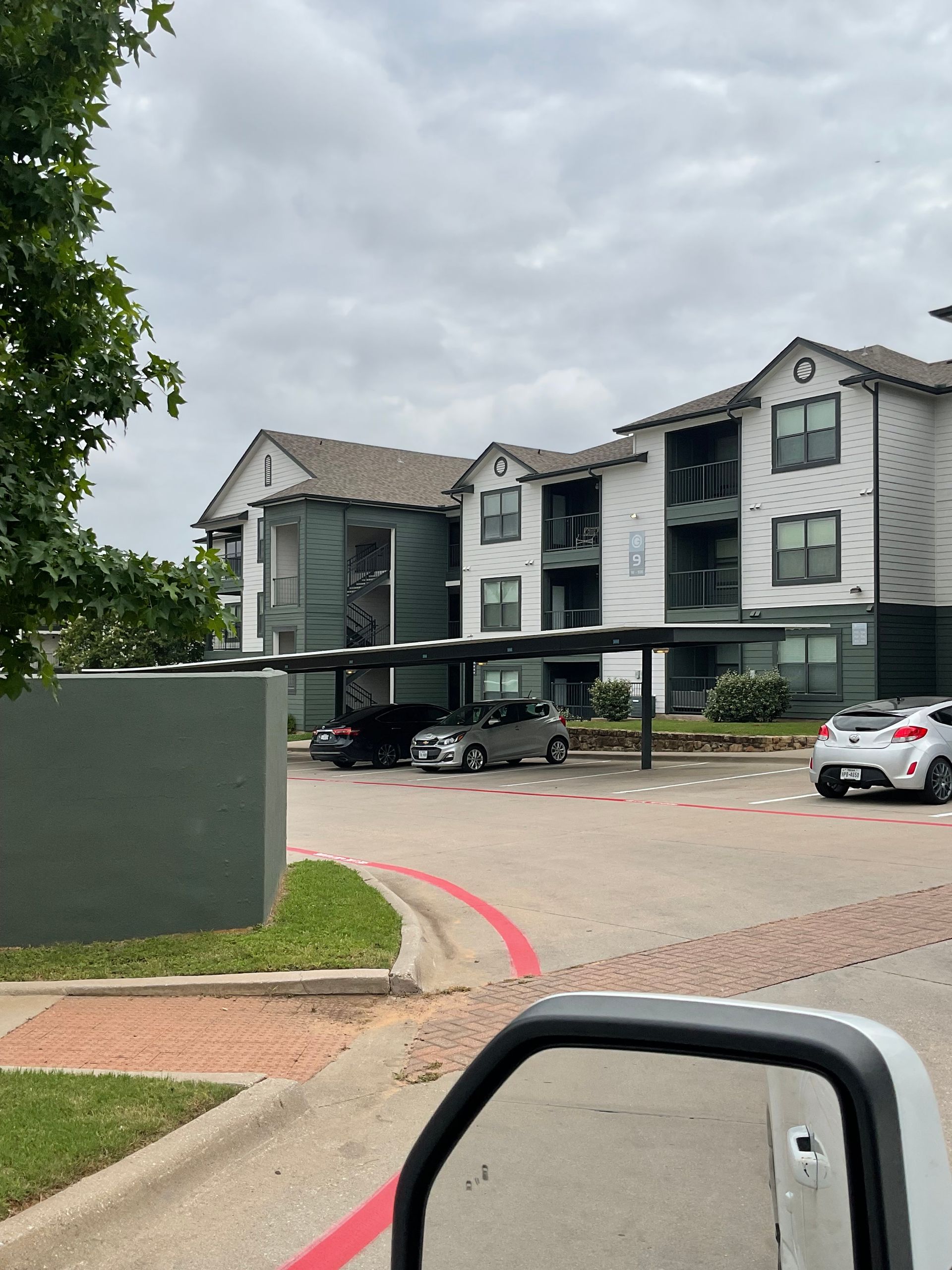 Apartment building exterior, white with teal accents, parking, cloudy sky.