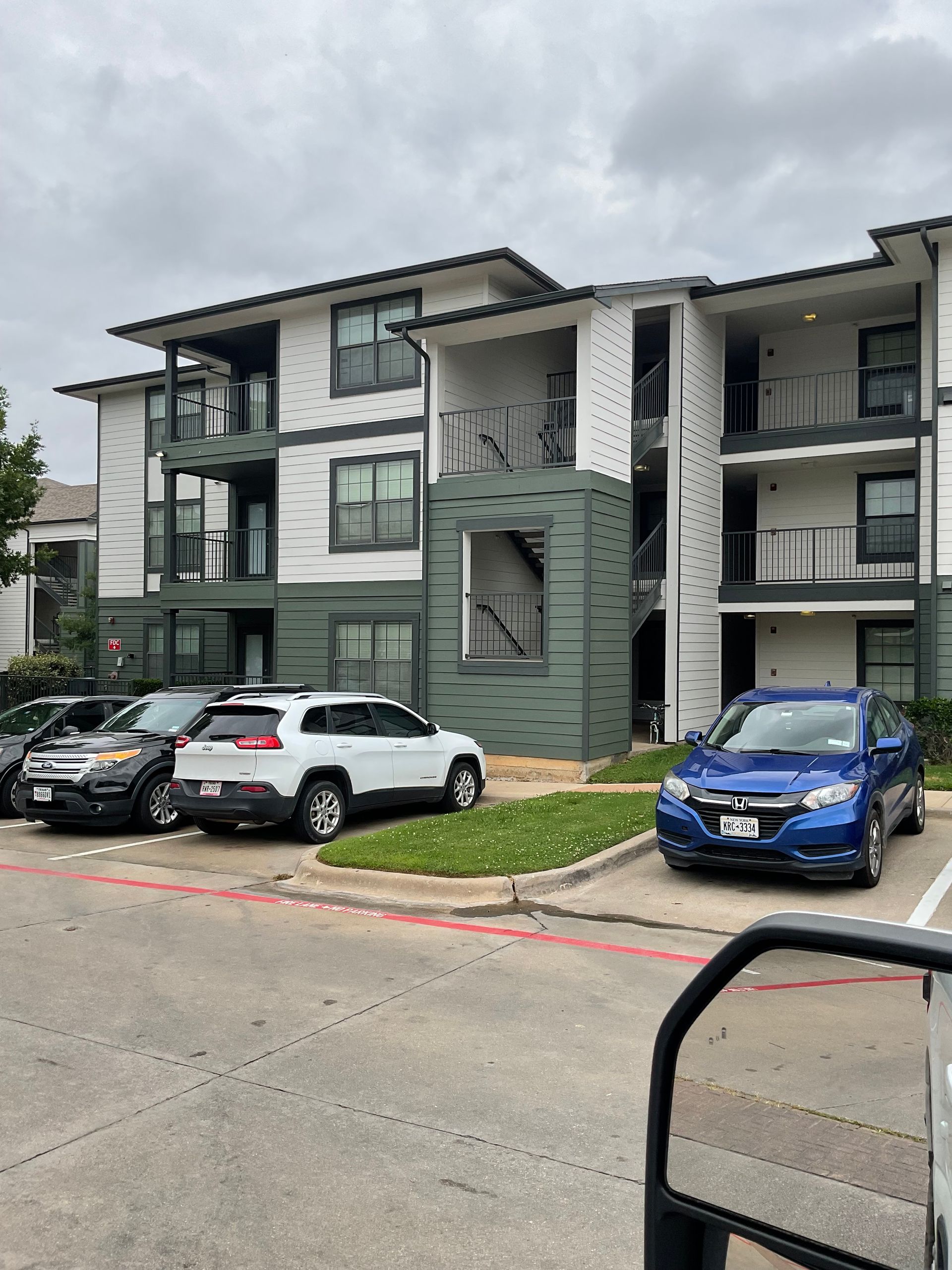 Apartment building with cars parked in front on a cloudy day. Exterior is white and green.