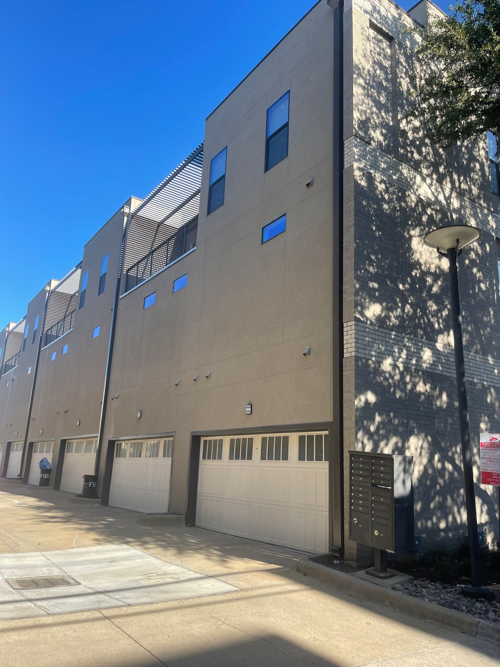 Modern townhouses with garage doors and balconies. Neutral colored exterior walls. Clear sky overhead.