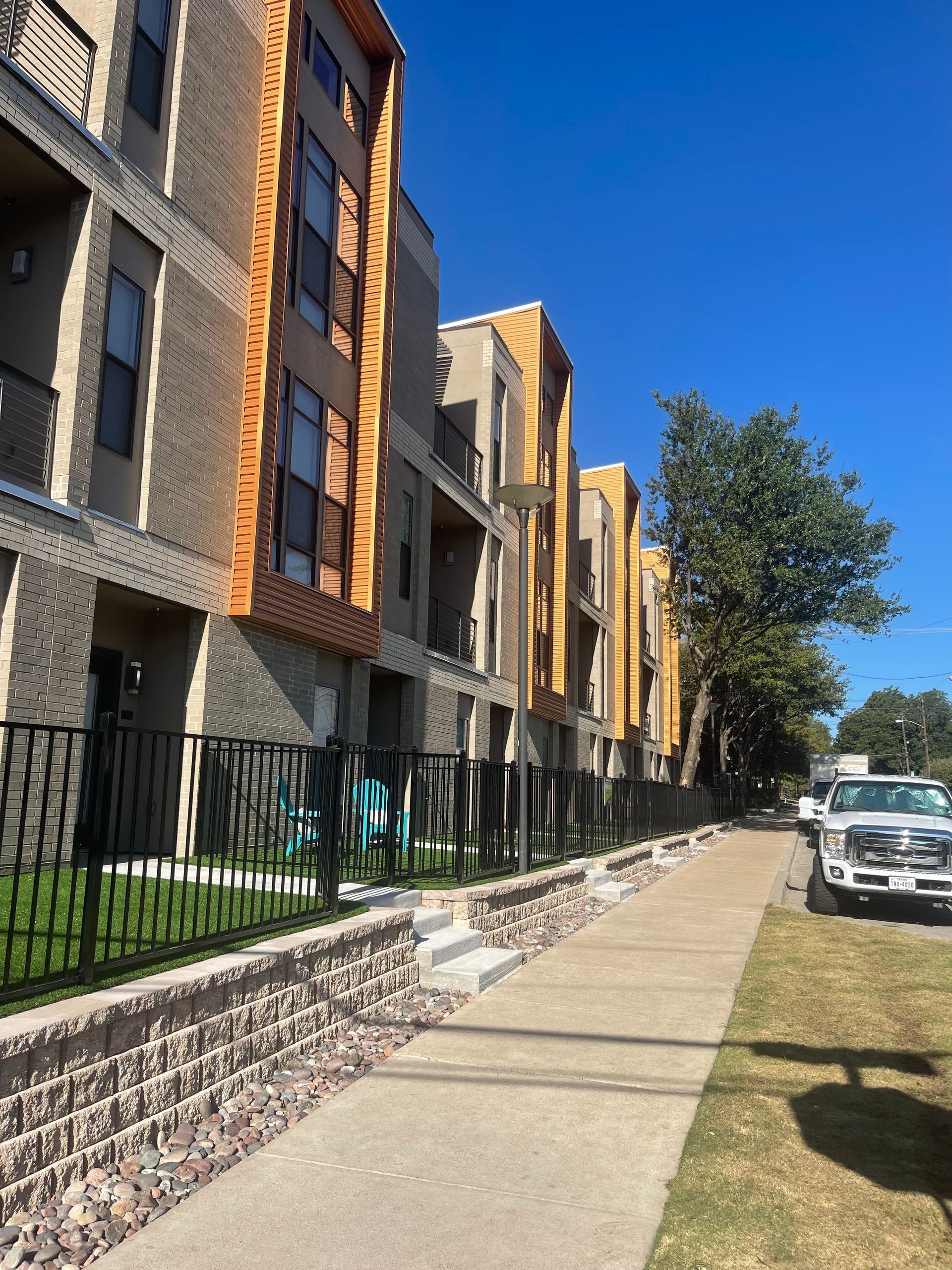 Apartment complex with a stone wall and sidewalk. Buildings are beige and brown.