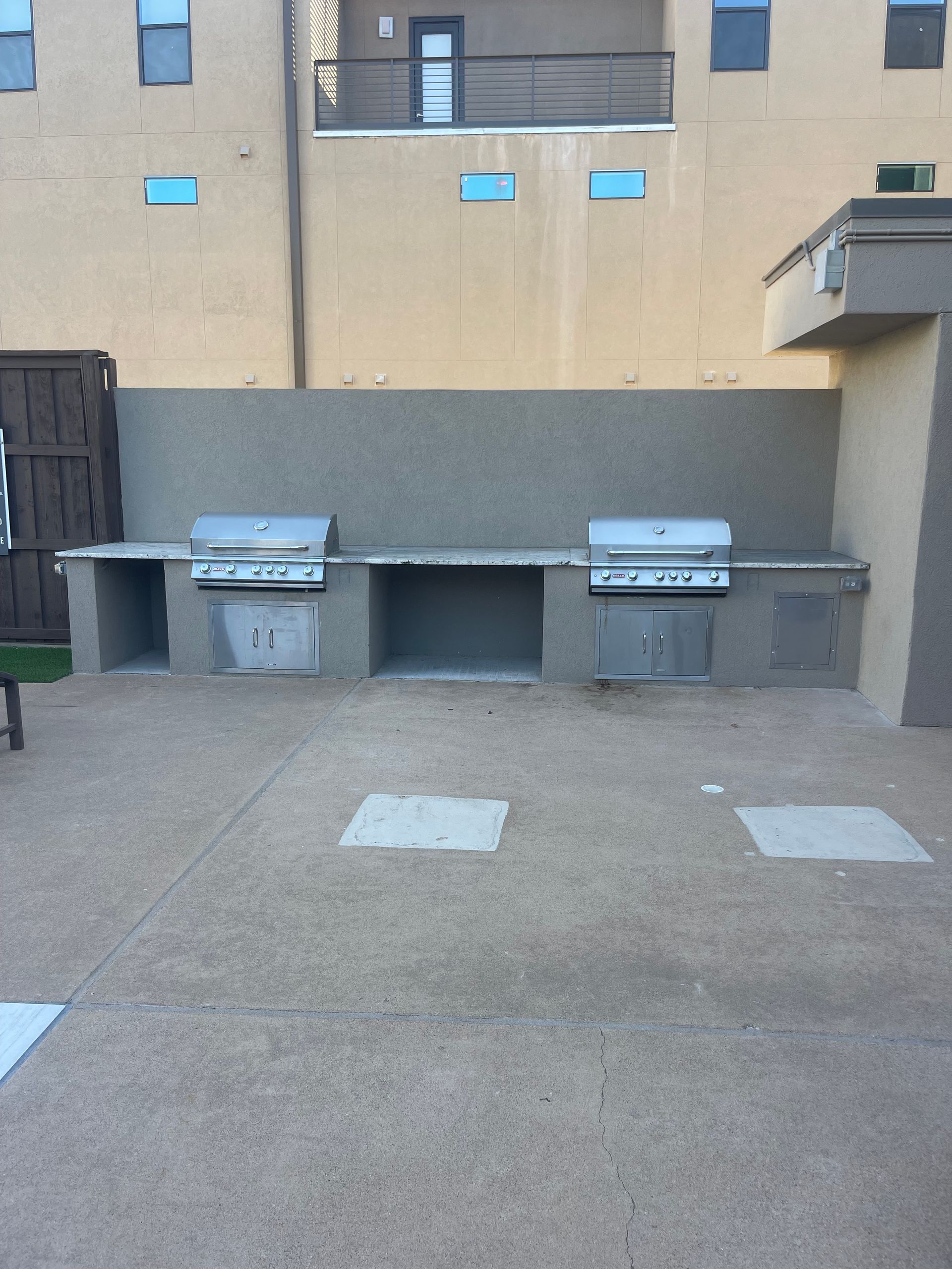 Outdoor grilling station with two built-in grills, concrete countertop, and open storage.