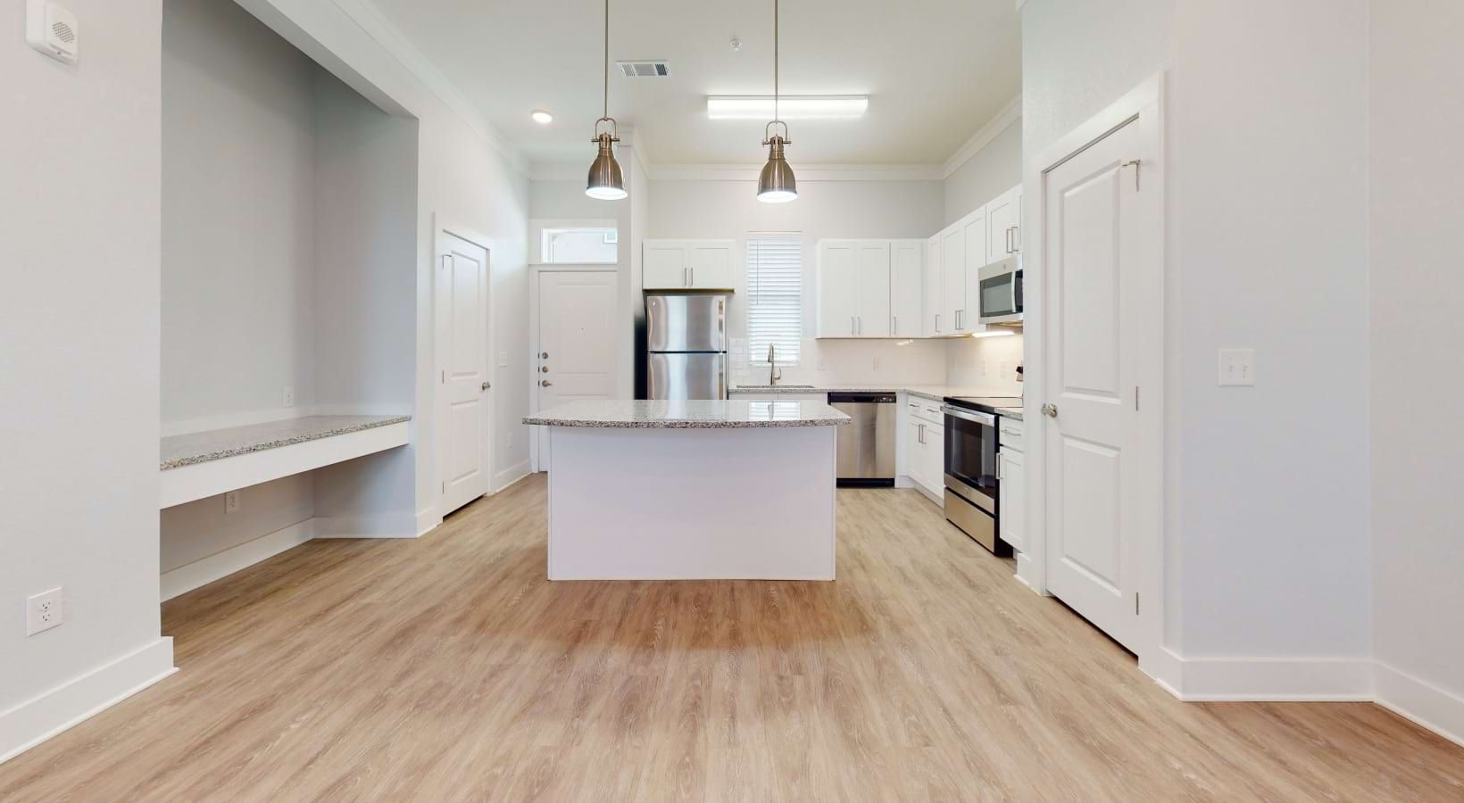 Modern kitchen with island, stainless steel appliances, white cabinets, and wood-look flooring.