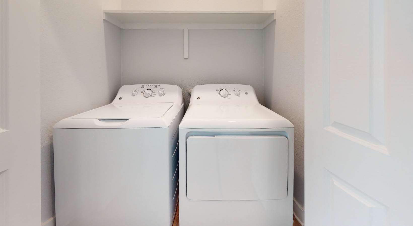 White washer and dryer in a small laundry closet with a shelf above.