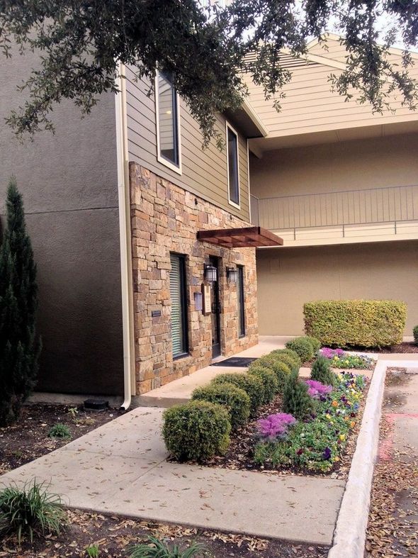 Two-story building with stone facade entrance, beige siding, walkway, and landscaped flower bed.