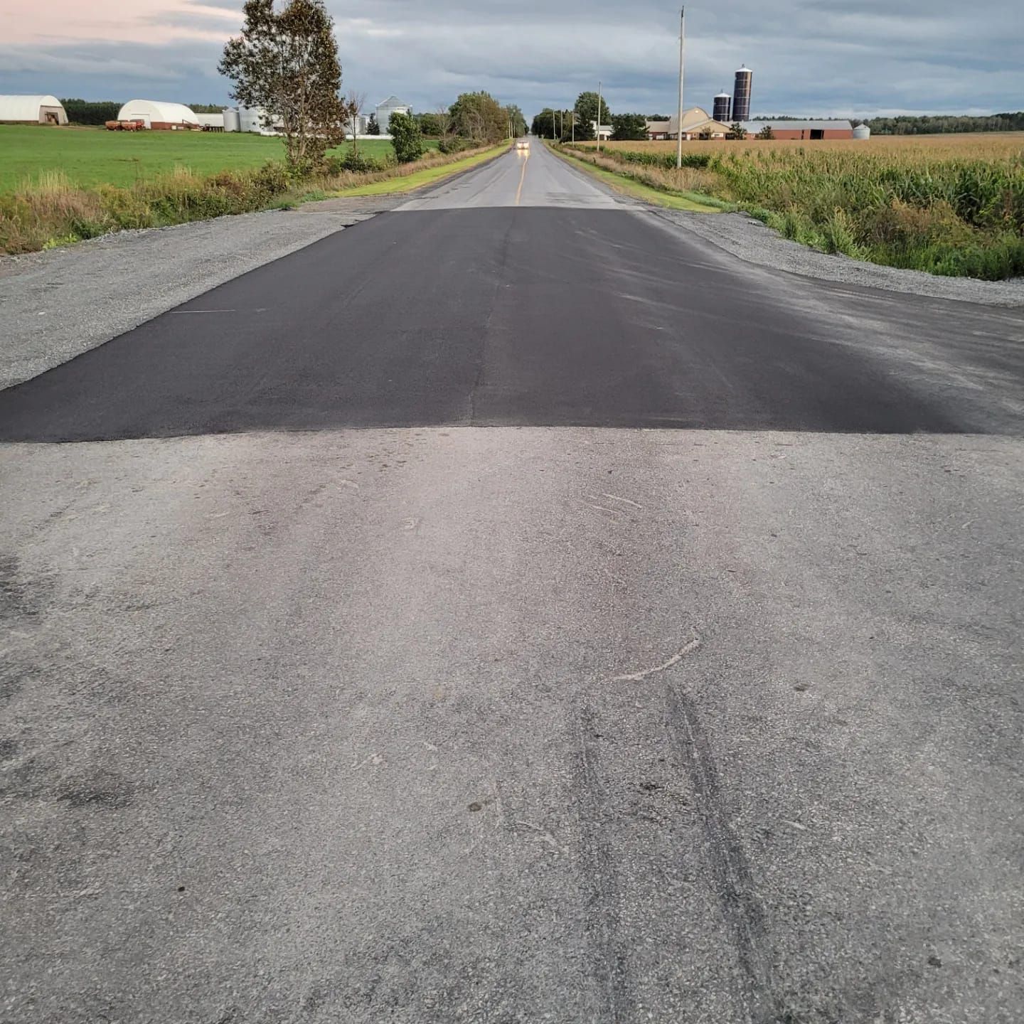 A newly paved road with a farm in the background.