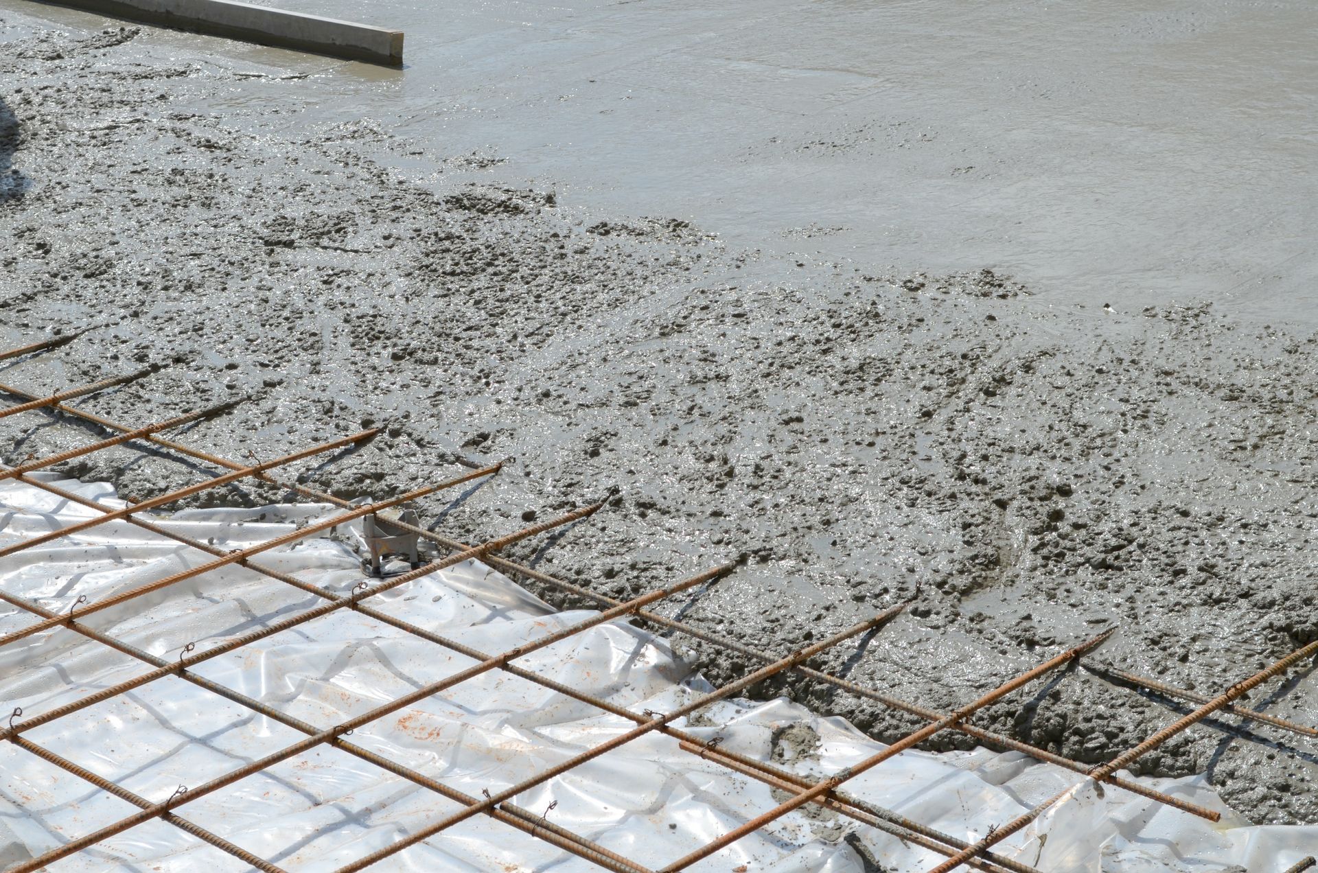 Fresh concrete being poured over a wire mesh reinforcement on a construction site.