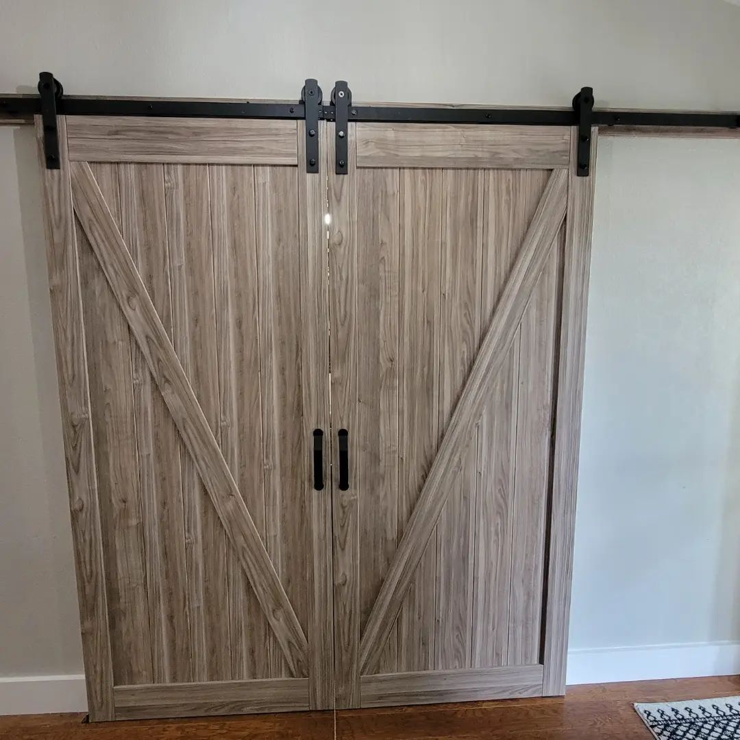 Two light-brown barn doors with black hardware and handles, sliding on a black track against a gray wall.