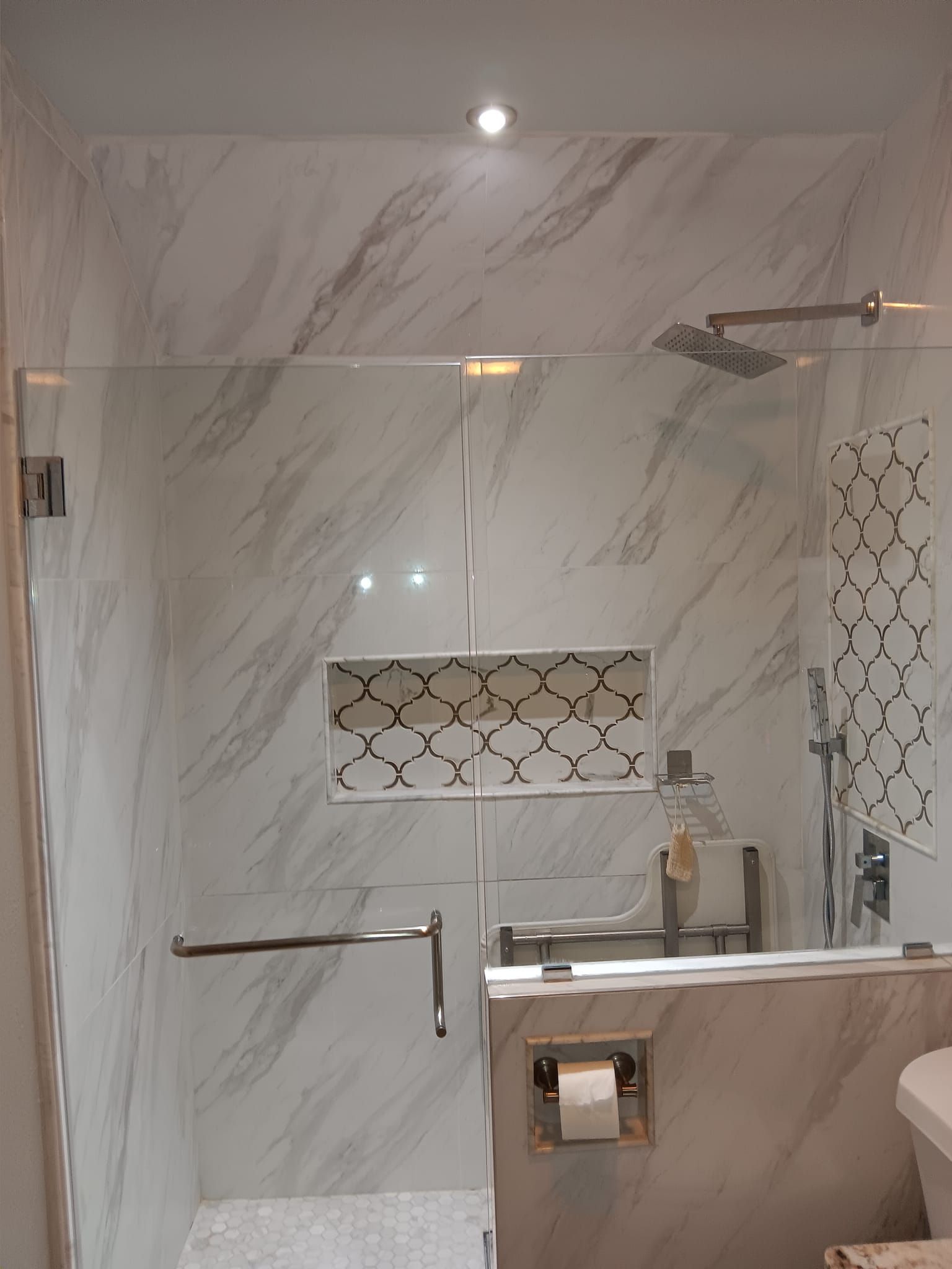 A modern, white-tiled shower with a glass door and decorative mosaic tile niche.
