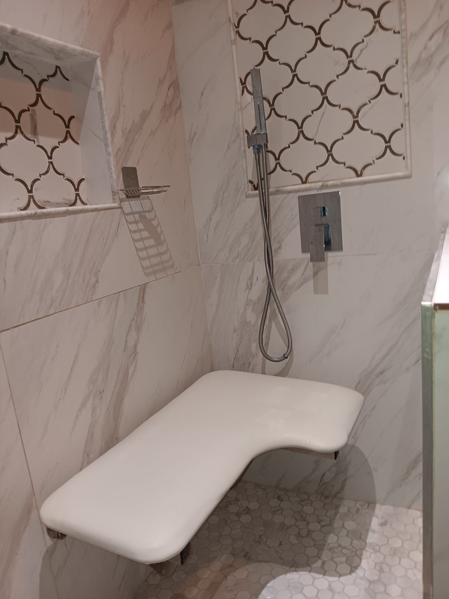 Shower with white tiled walls, built-in seat, and a handheld showerhead.