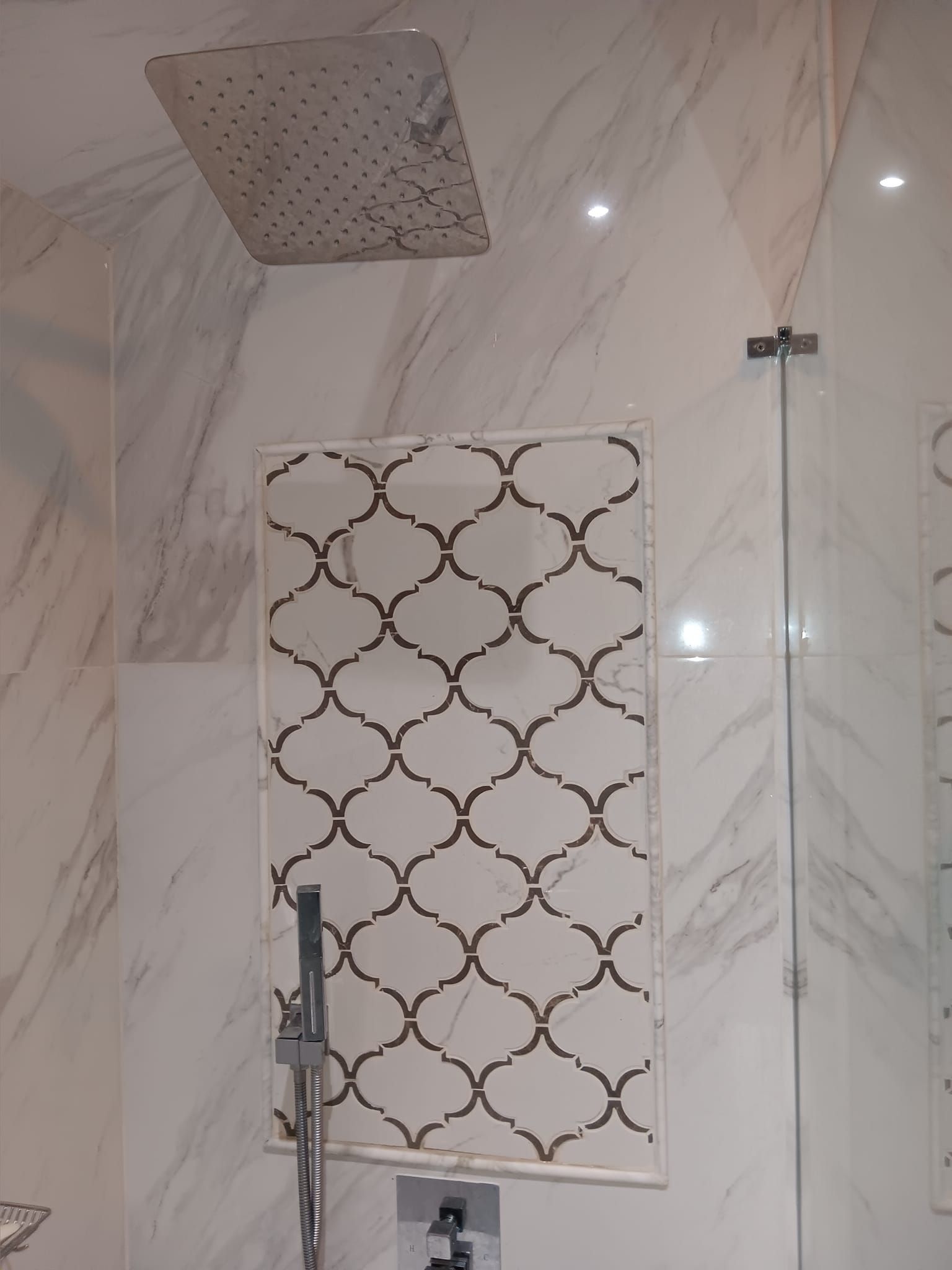 Shower with marble walls, patterned niche, and large square showerhead.