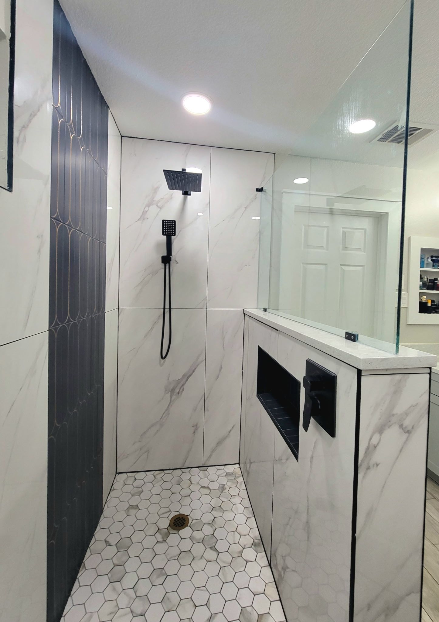 Modern shower with white marble tiles, black fixtures, and a glass door.
