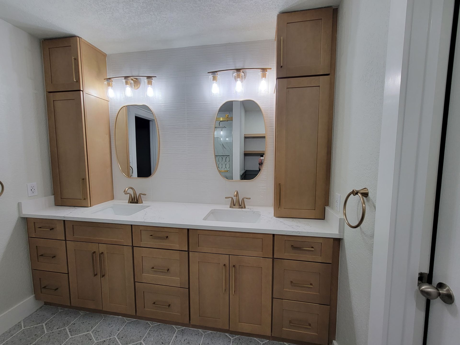 Bathroom with double vanity, oval mirrors, tall cabinets, and light-colored cabinets and countertops.