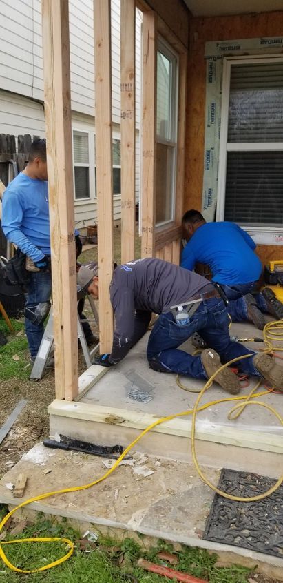 Construction workers building a porch frame on a concrete step. One man stands, two kneel.