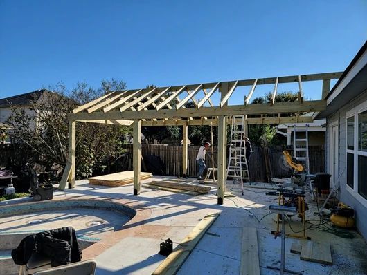 A wooden pergola being built in a backyard near a pool, with tools and a ladder visible.