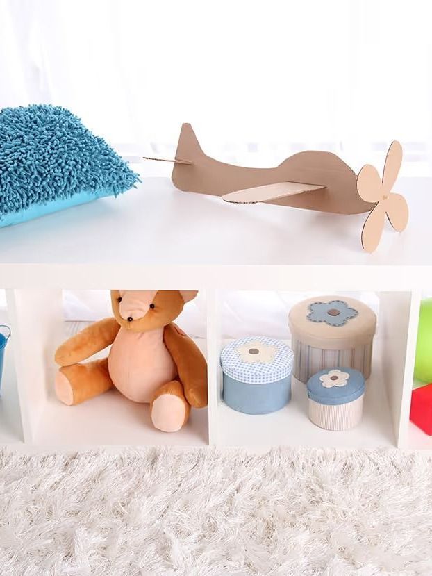 A teddy bear is sitting on a shelf next to a cardboard airplane