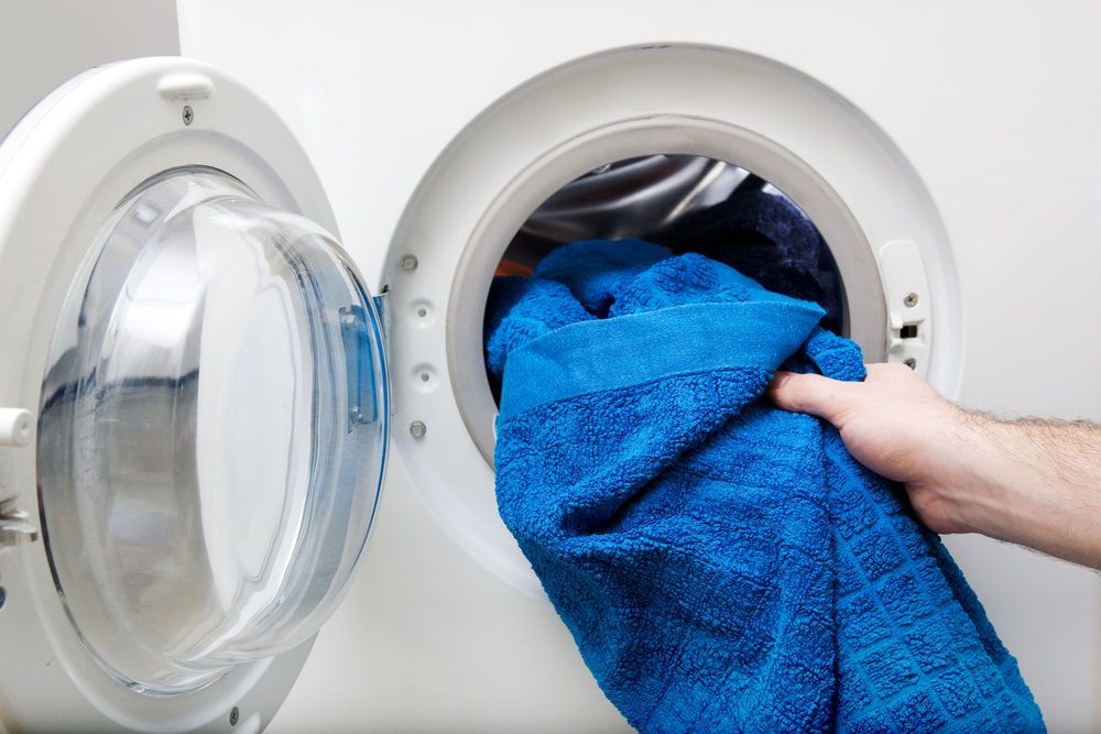 A Person Is Taking A Blue Towel Out Of A Washing Machine — Tanilba Bay Laundromat In Tanilba Bay, NSW