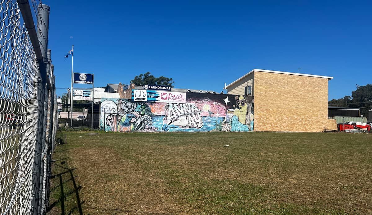 A Building With Graffiti On The Side Of It Is Behind A Chain Link Fence — Tanilba Bay Laundromat In Tanilba Bay, NSW