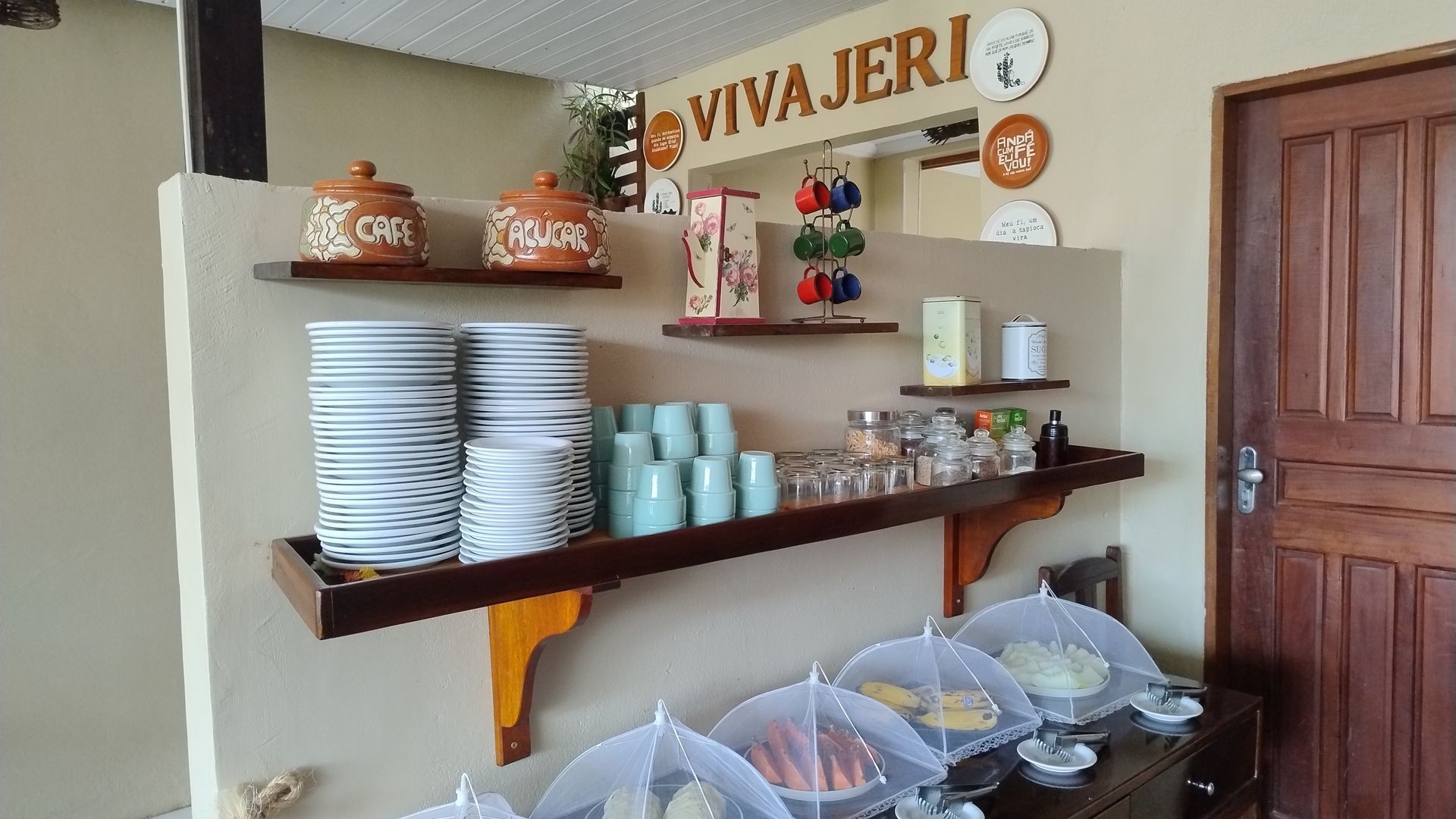 Mesa de café da manhã posta com torradas, frutas, café, ovos e uma piscina ao fundo.