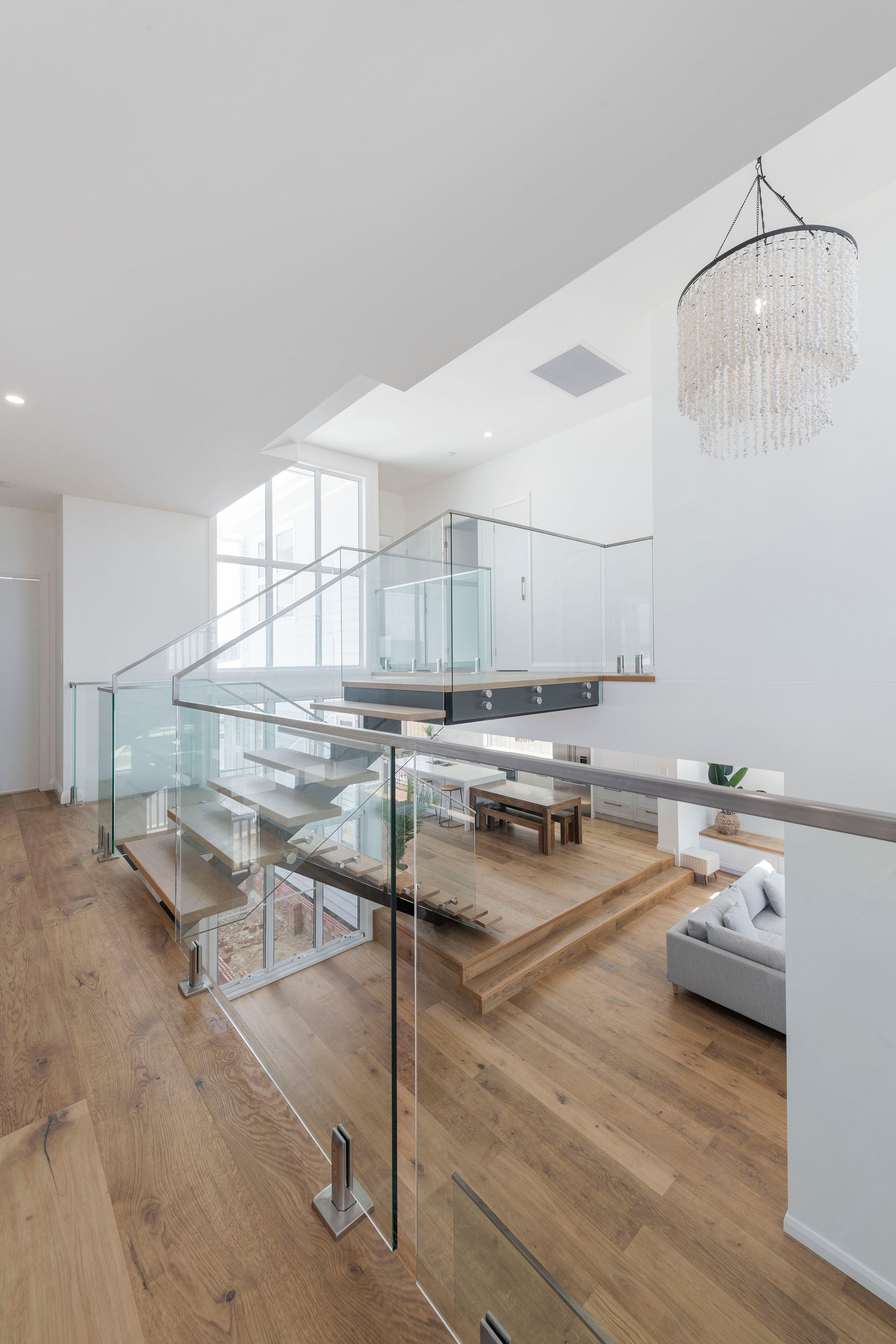 Modern Home Interior With Glass Railings, Wooden Stairs, and Chandelier — Indie Living In Lake Macquarie, NSW